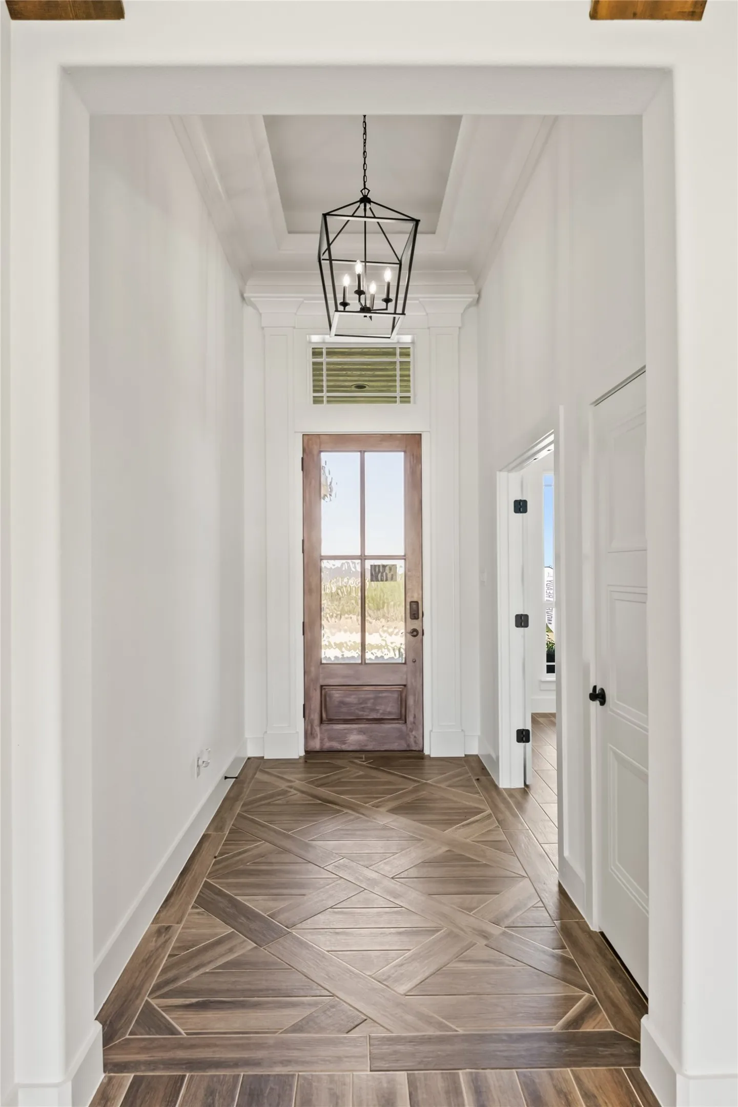 Entryway featuring wood-finish flooring with a decorative pattern, a wood-finish door with glass panels, a transom window, and a coffered ceiling with a black lantern-style chandelier