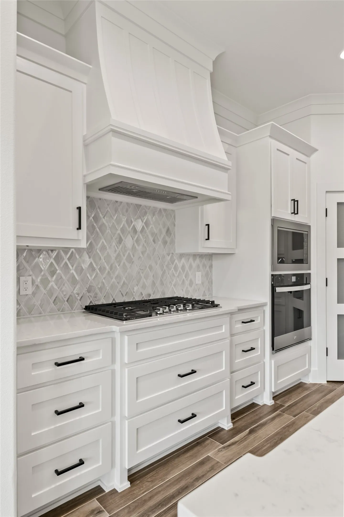 White shaker cabinetry with black hardware, gas cooktop, built-in double ovens, and wood-finish flooring