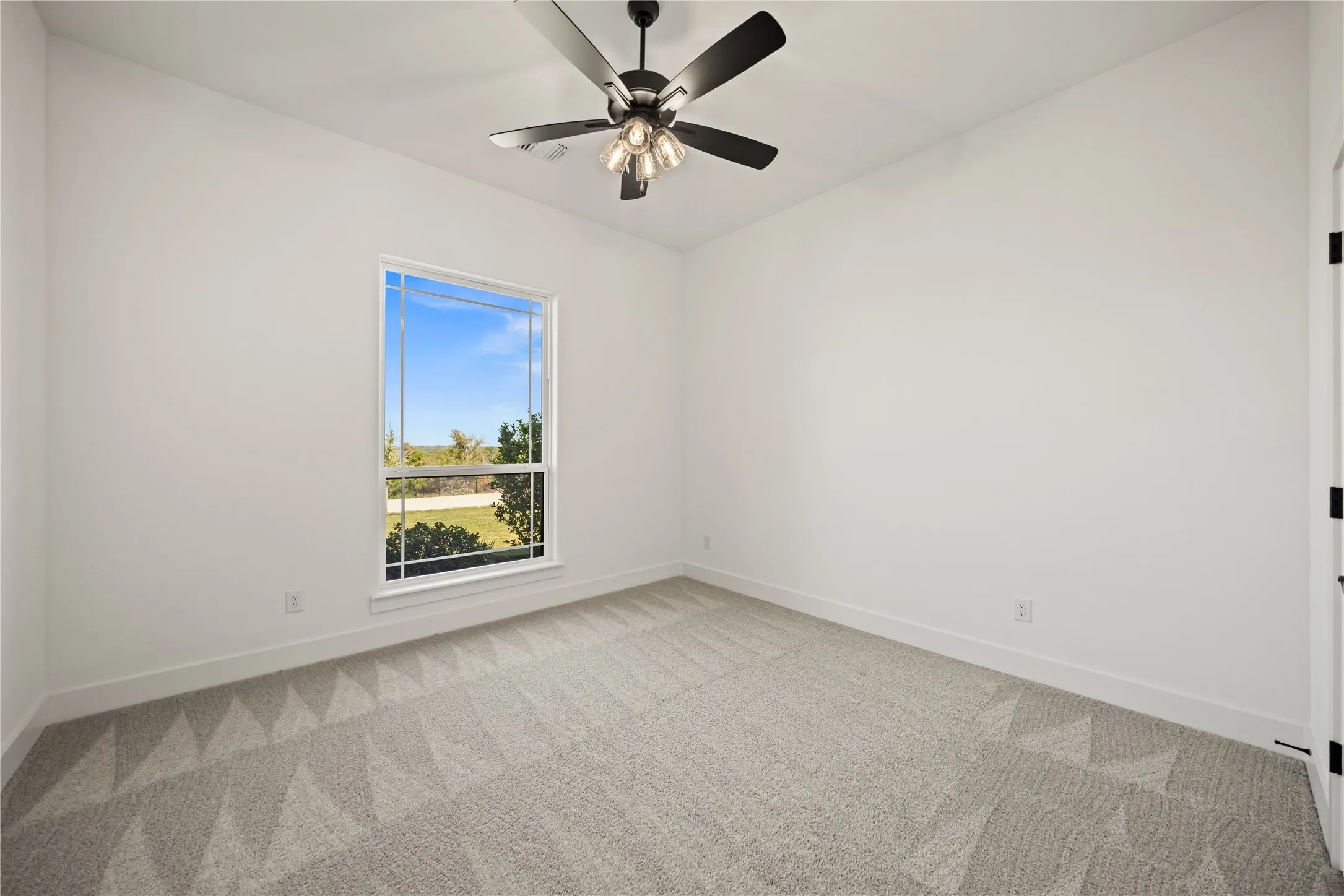 Bright room featuring a ceiling fan with integrated lighting, a large window, white walls, and patterned carpet flooring