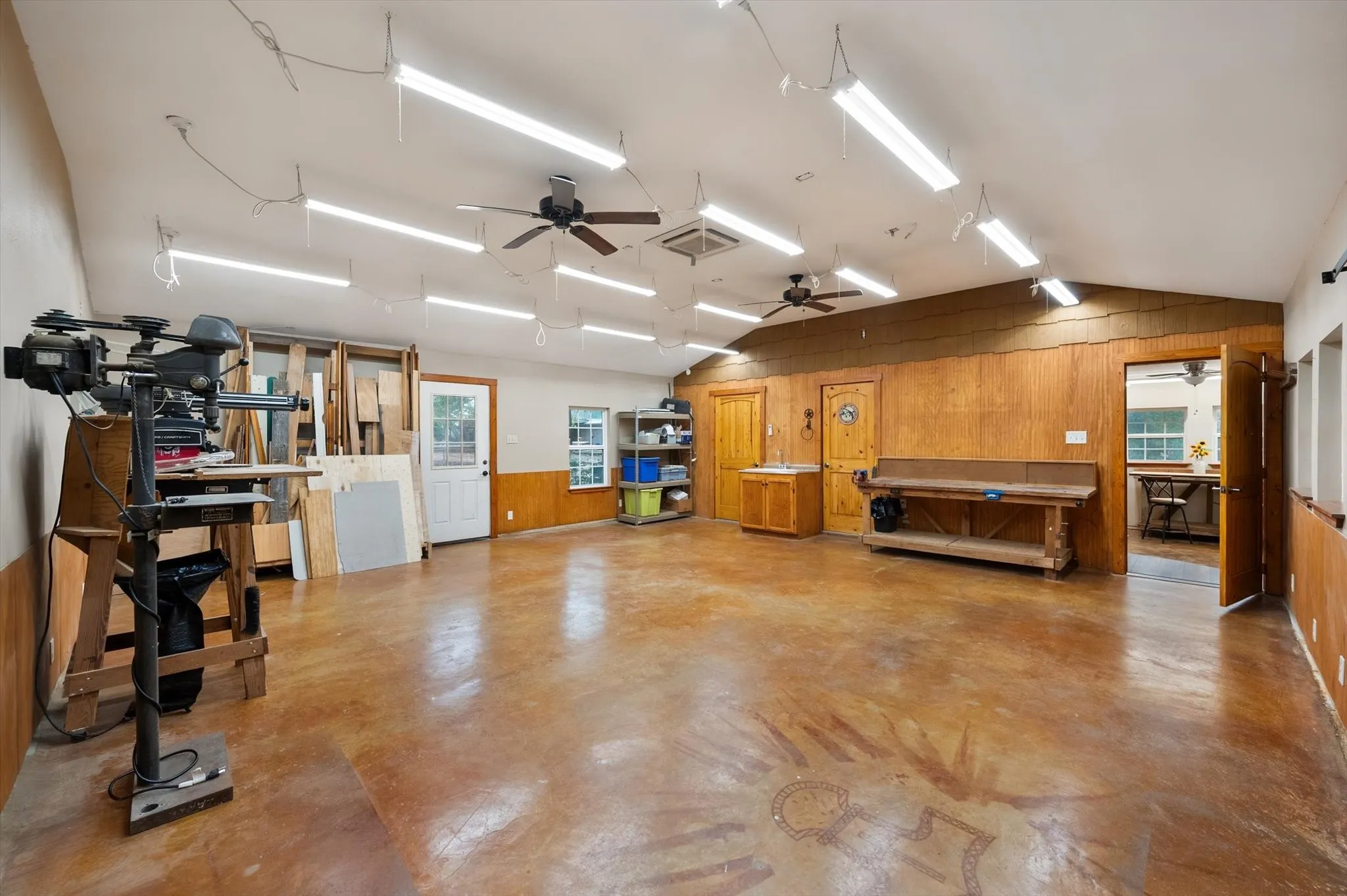 Spacious room featuring a vaulted ceiling with multiple ceiling fans and strip lighting, wood-paneled walls, and a stained concrete floor