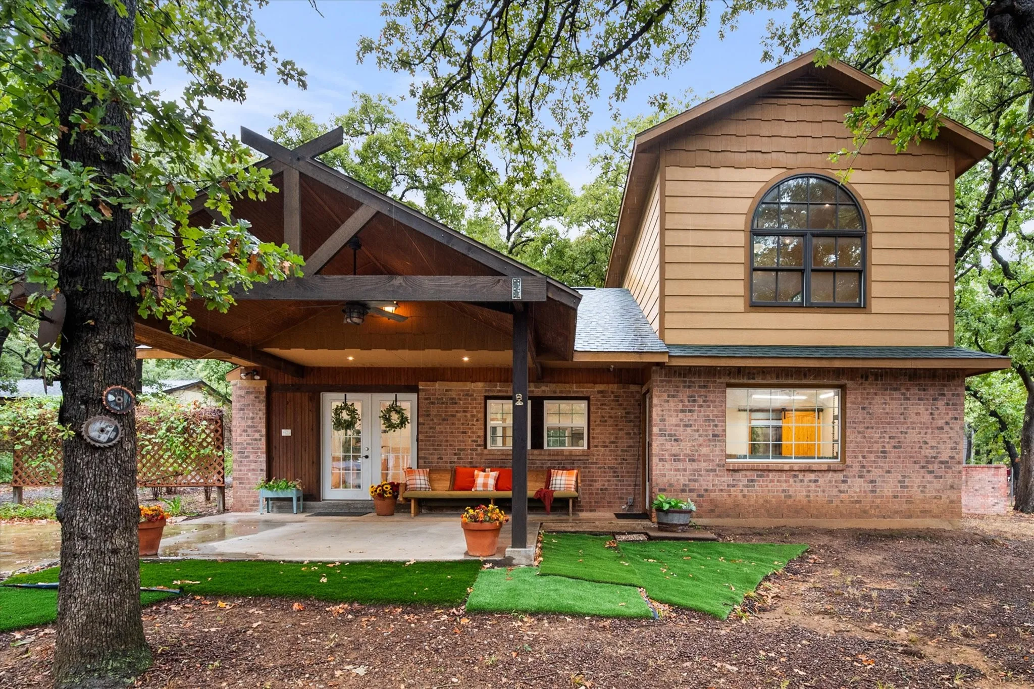 Brick exterior with wood siding, arched window, covered patio, and French doors