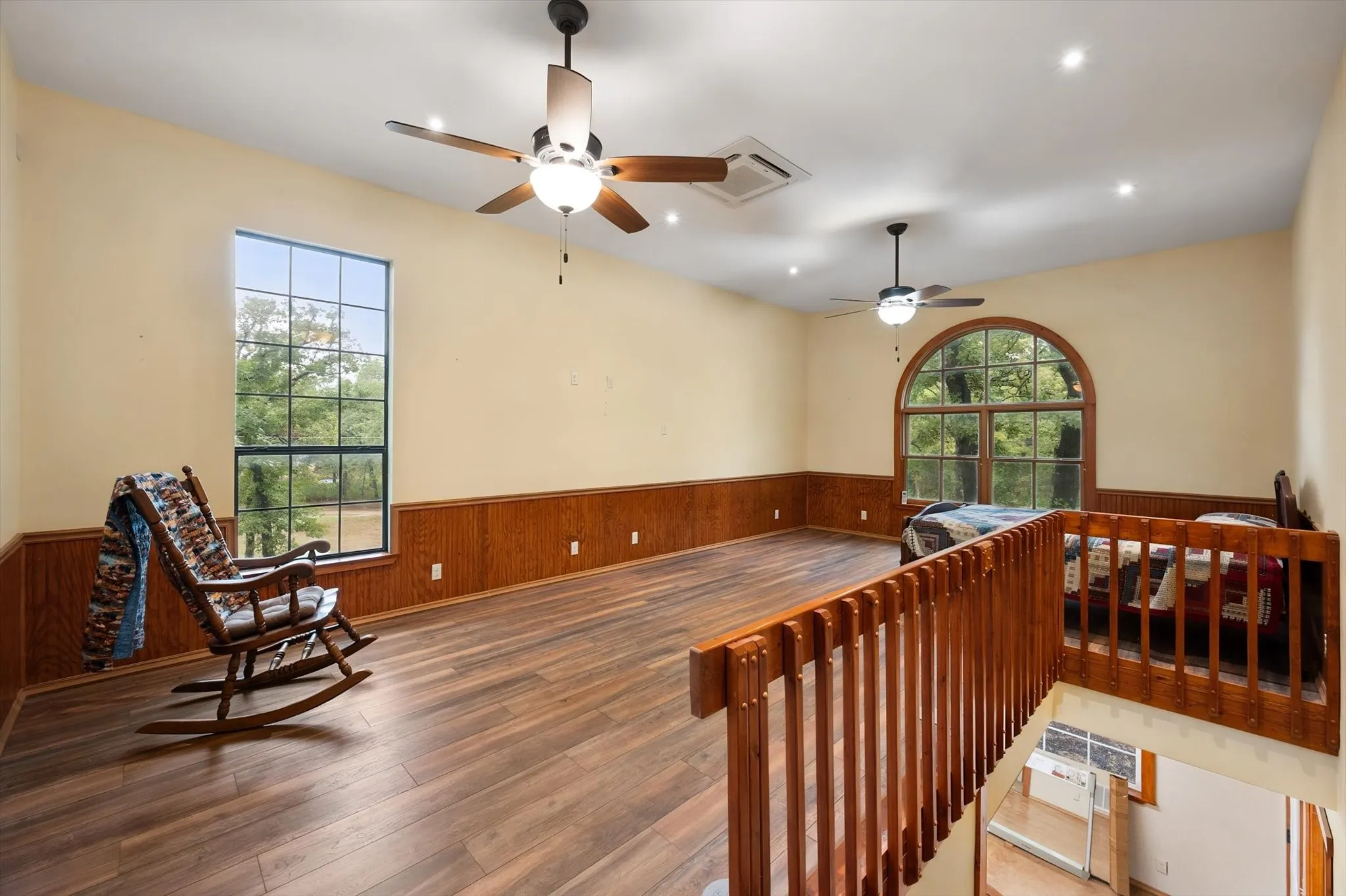 Wood-finish flooring, wood paneling, recessed lighting, ceiling fans, and an arched window