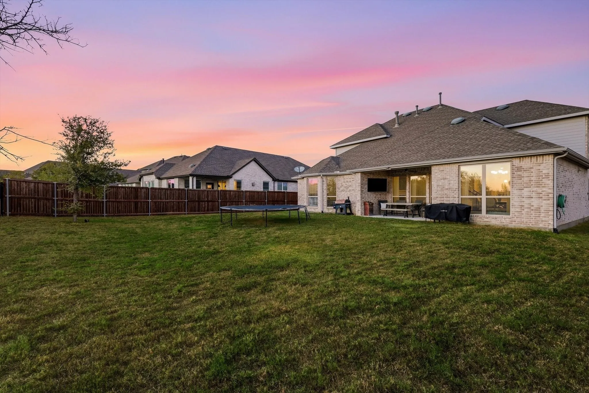 Expansive backyard with a manicured lawn, brick exterior, and covered patio space