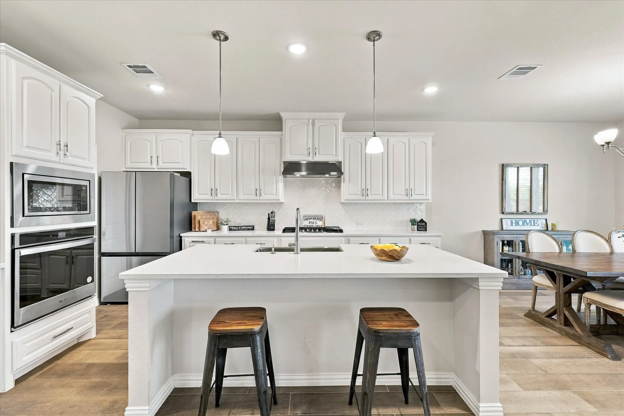 White cabinetry, stainless steel appliances, white countertop island with pendant lighting, tile backsplash, and wood-finish flooring