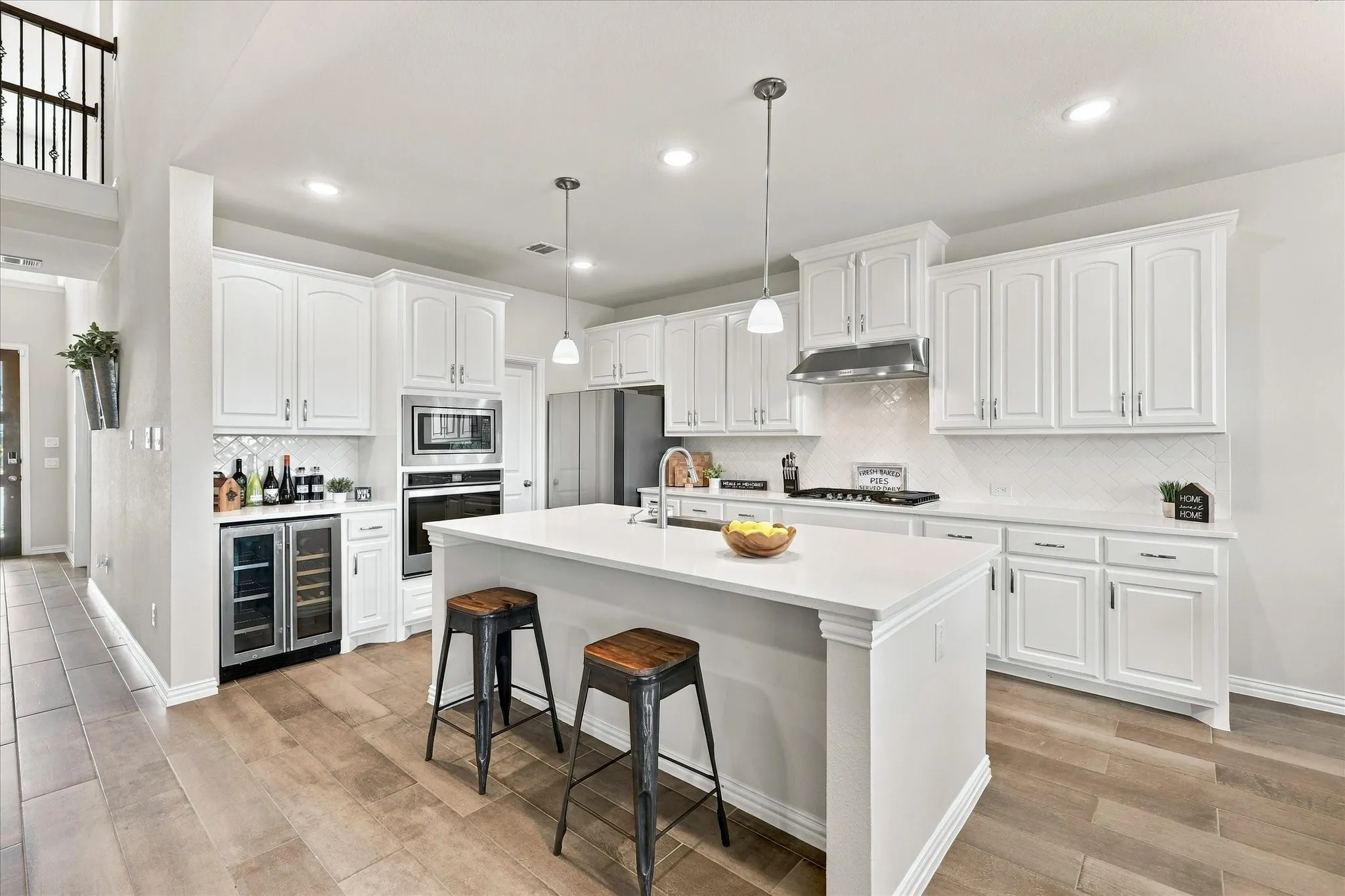 White cabinetry with stainless steel appliances, recessed lighting, and a center island with pendant lighting