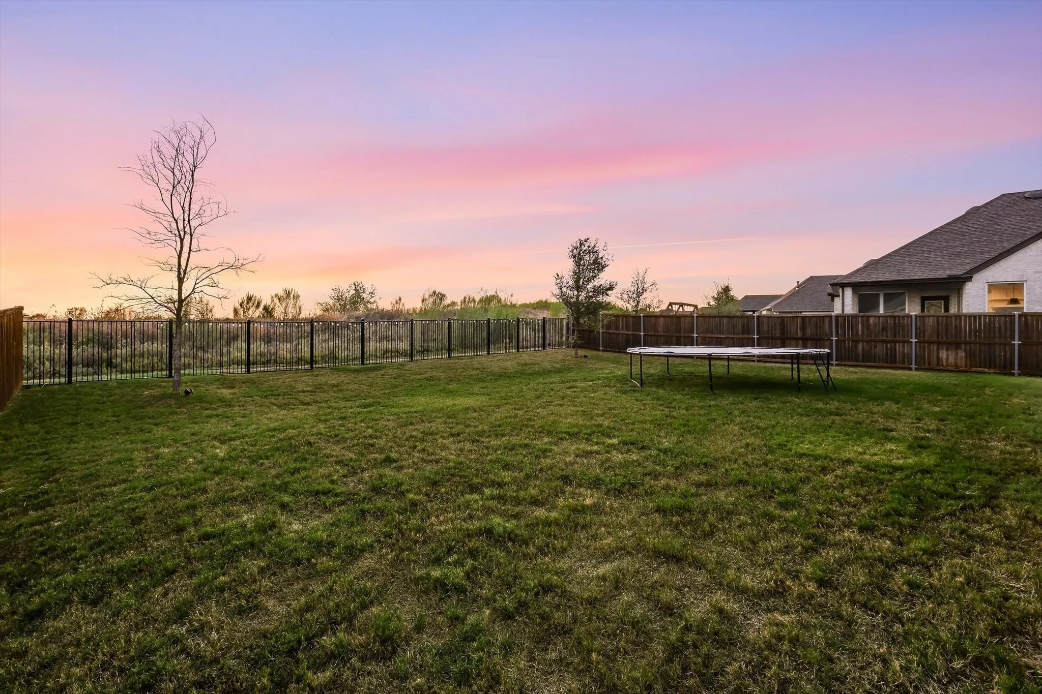 Expansive green lawn with a wood fence and a black metal fence