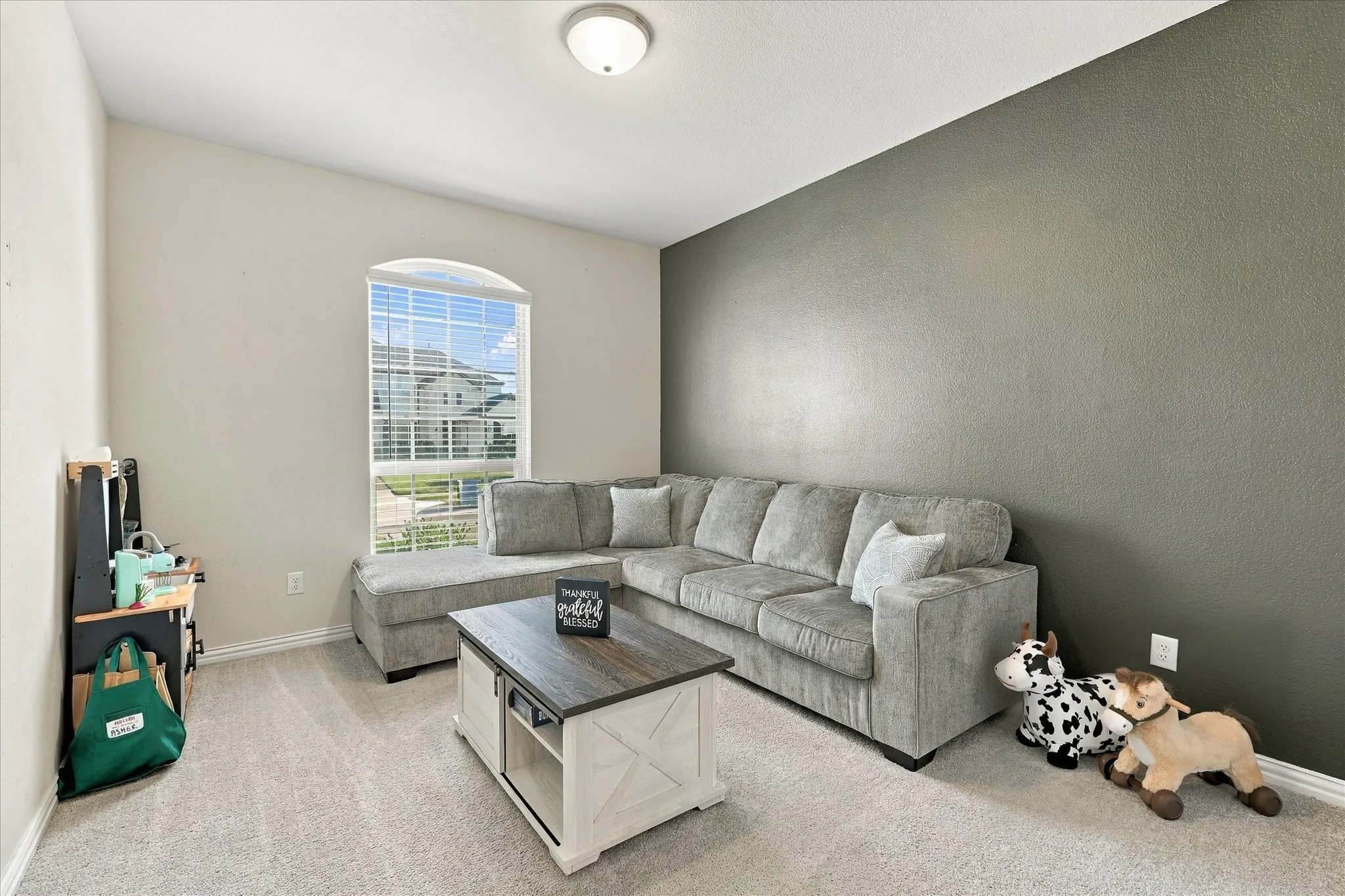 Vaulted ceiling, arched window with blinds, accent wall, and light-toned carpeting