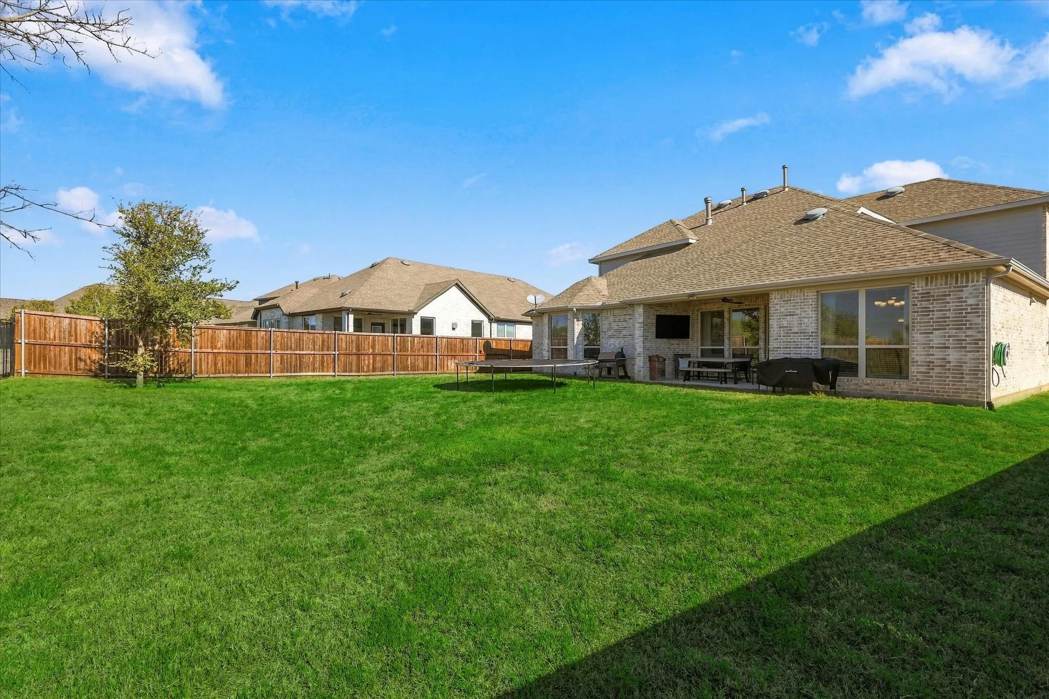 Expansive fenced backyard with a manicured lawn, brick exterior, and a covered patio