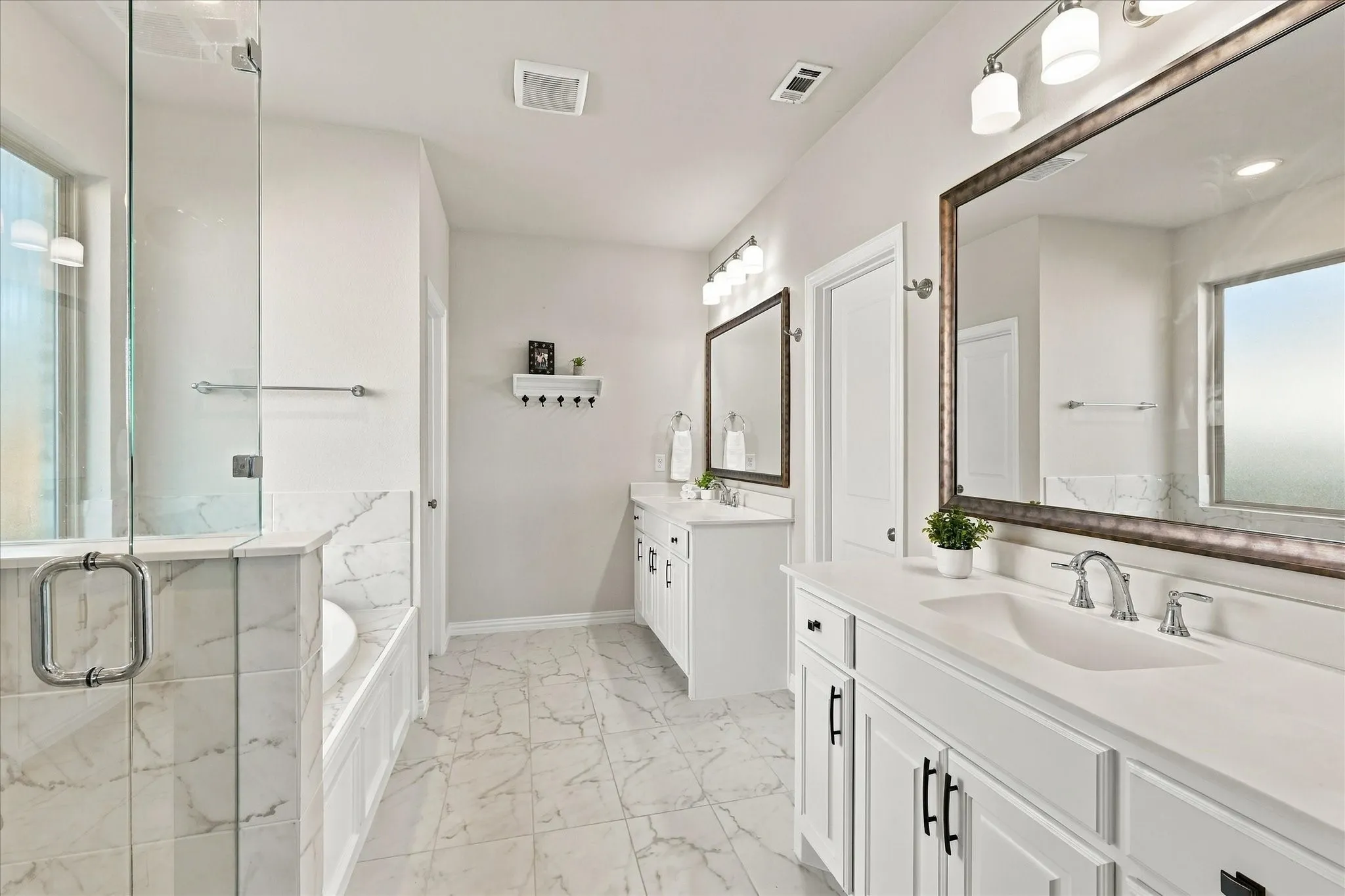 White cabinetry with black hardware, dual vanities, large framed mirrors, and a glass-enclosed shower with a separate tub