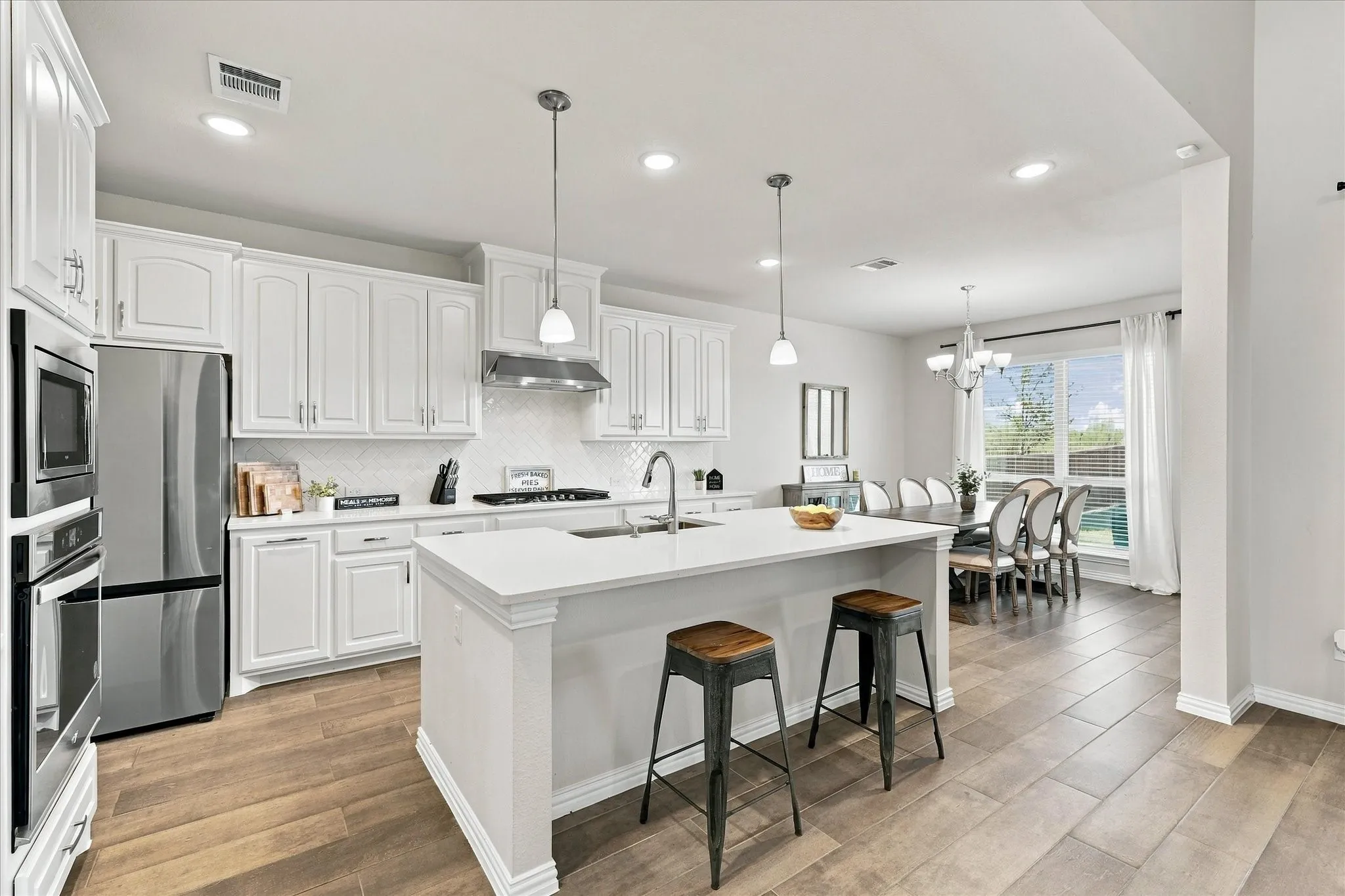 White cabinetry, stainless steel appliances, kitchen island with seating, wood-finish flooring, and a dining area with a chandelier