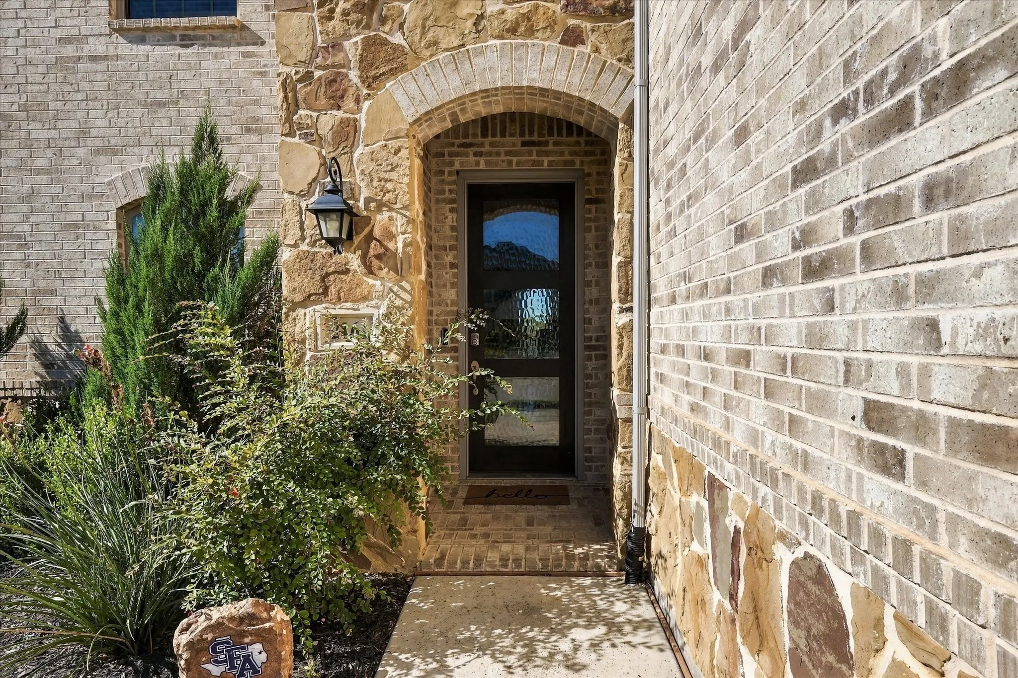 Arched stone entry with a paneled glass door, exterior sconce lighting, and decorative brick accents