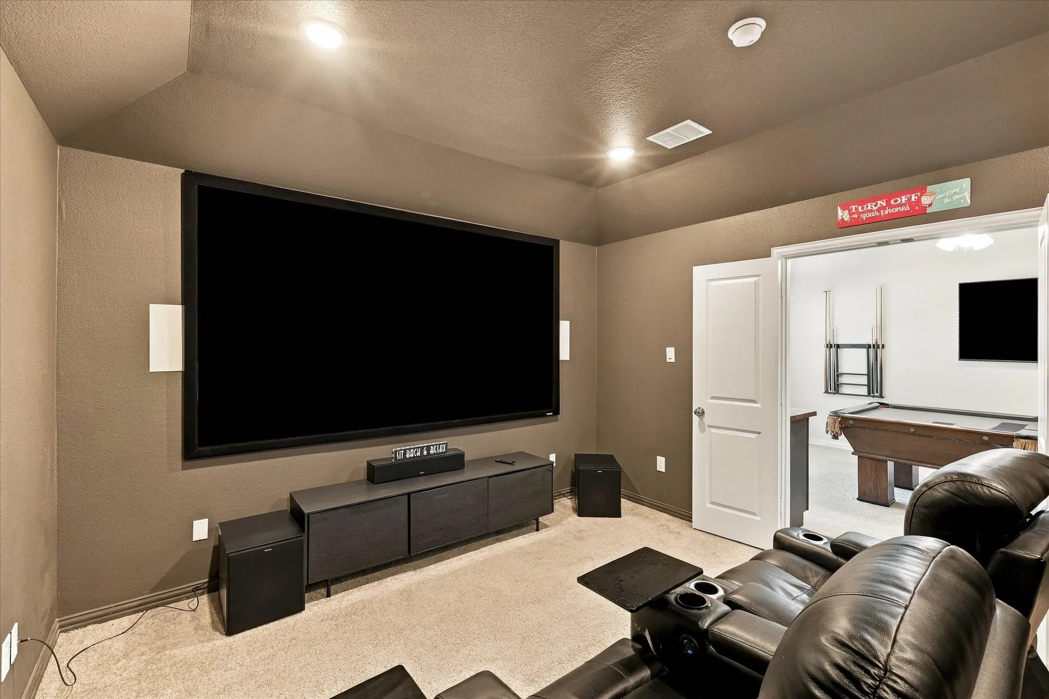 Dedicated media room featuring a large projection screen, recessed lighting, and soft carpeting