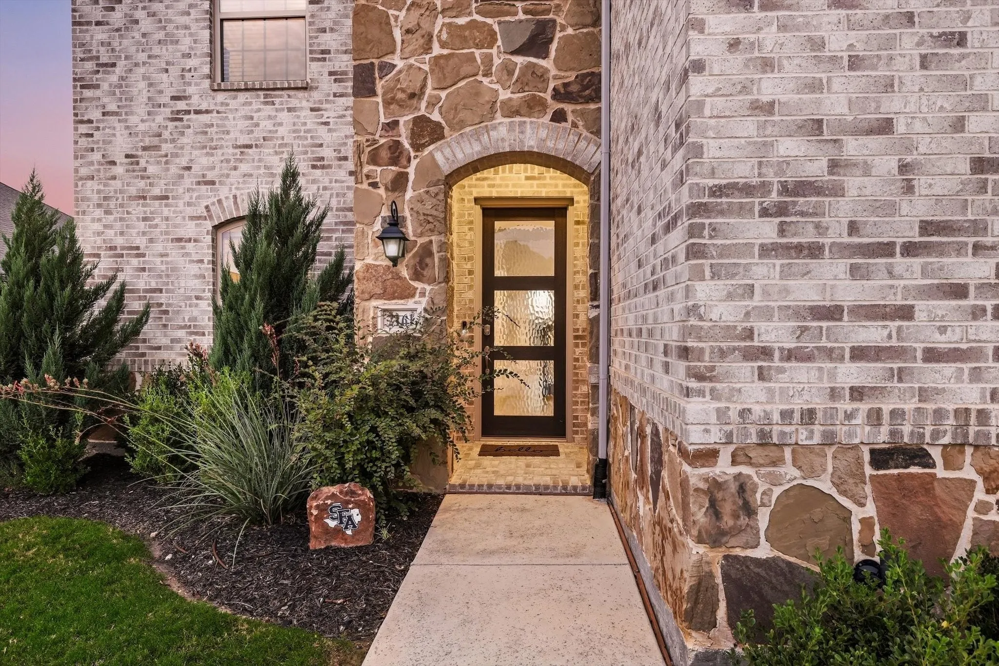 Stone and brick facade with an arched entryway, featuring a modern door with decorative glass panels and an exterior sconce