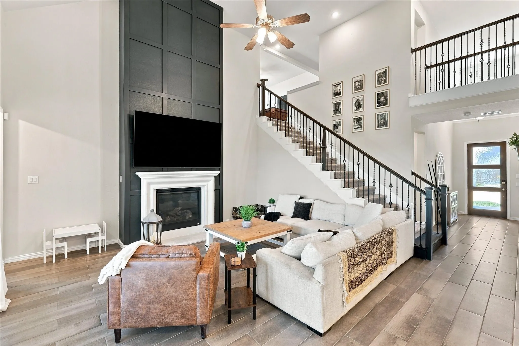 Two-story living area with high ceilings, feature wall with fireplace, recessed lighting, and a grand staircase with wrought iron balusters