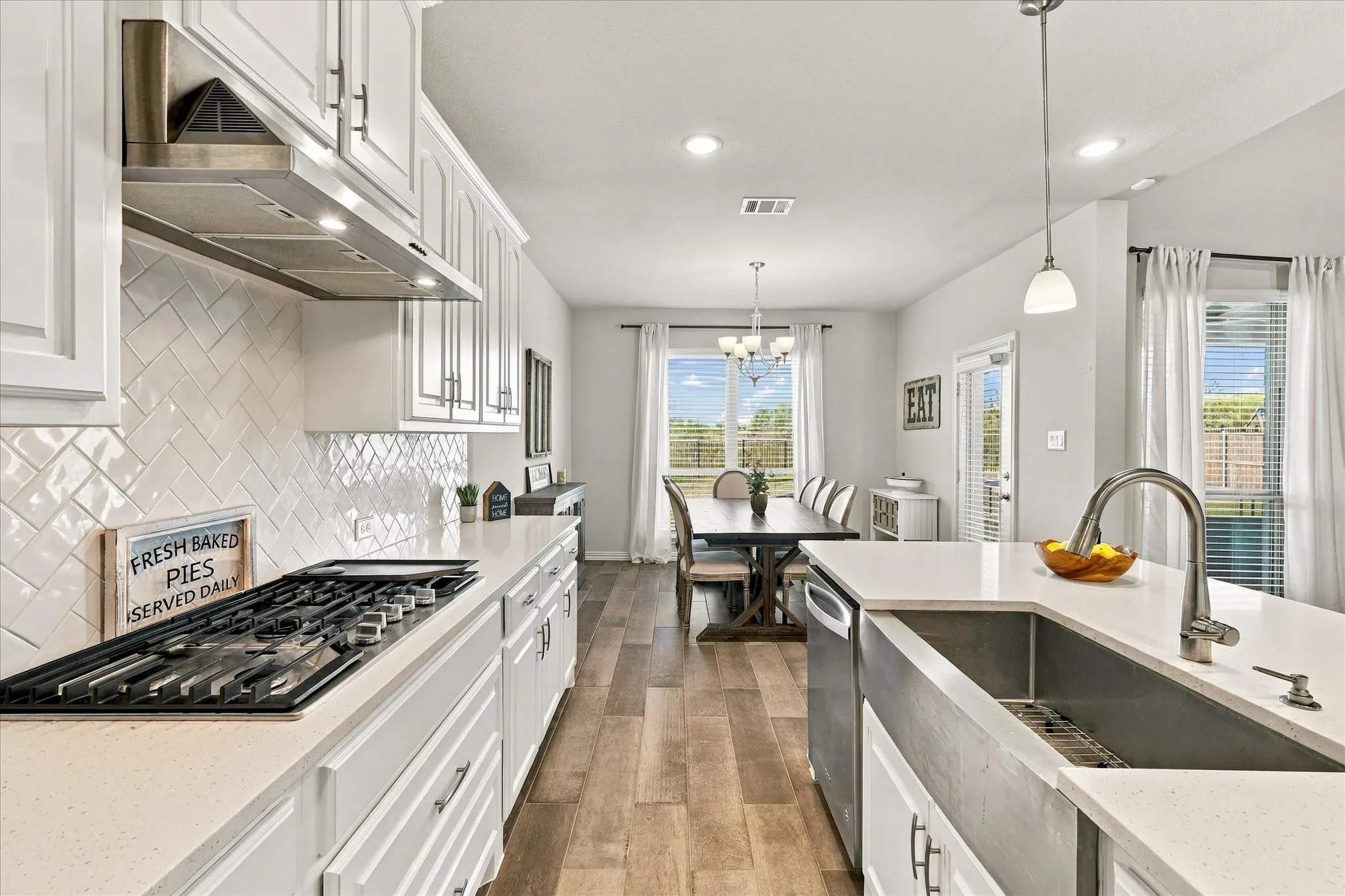 White shaker cabinetry with black hardware, herringbone tile backsplash, stainless steel range hood, built-in gas cooktop, and wood-finish flooring
