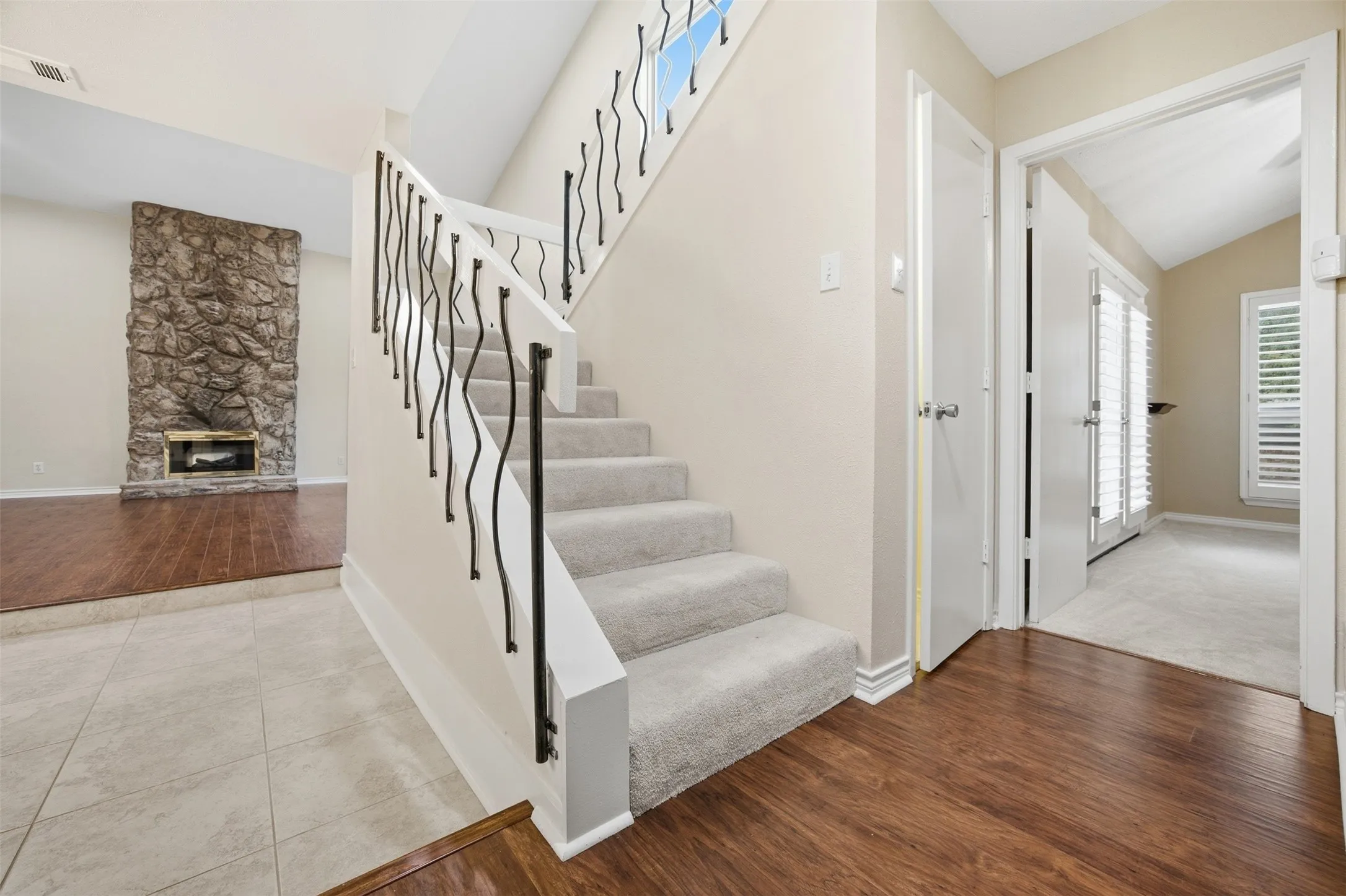 Carpeted staircase with decorative iron railings, tile flooring, wood-finish flooring, and a stone-clad fireplace