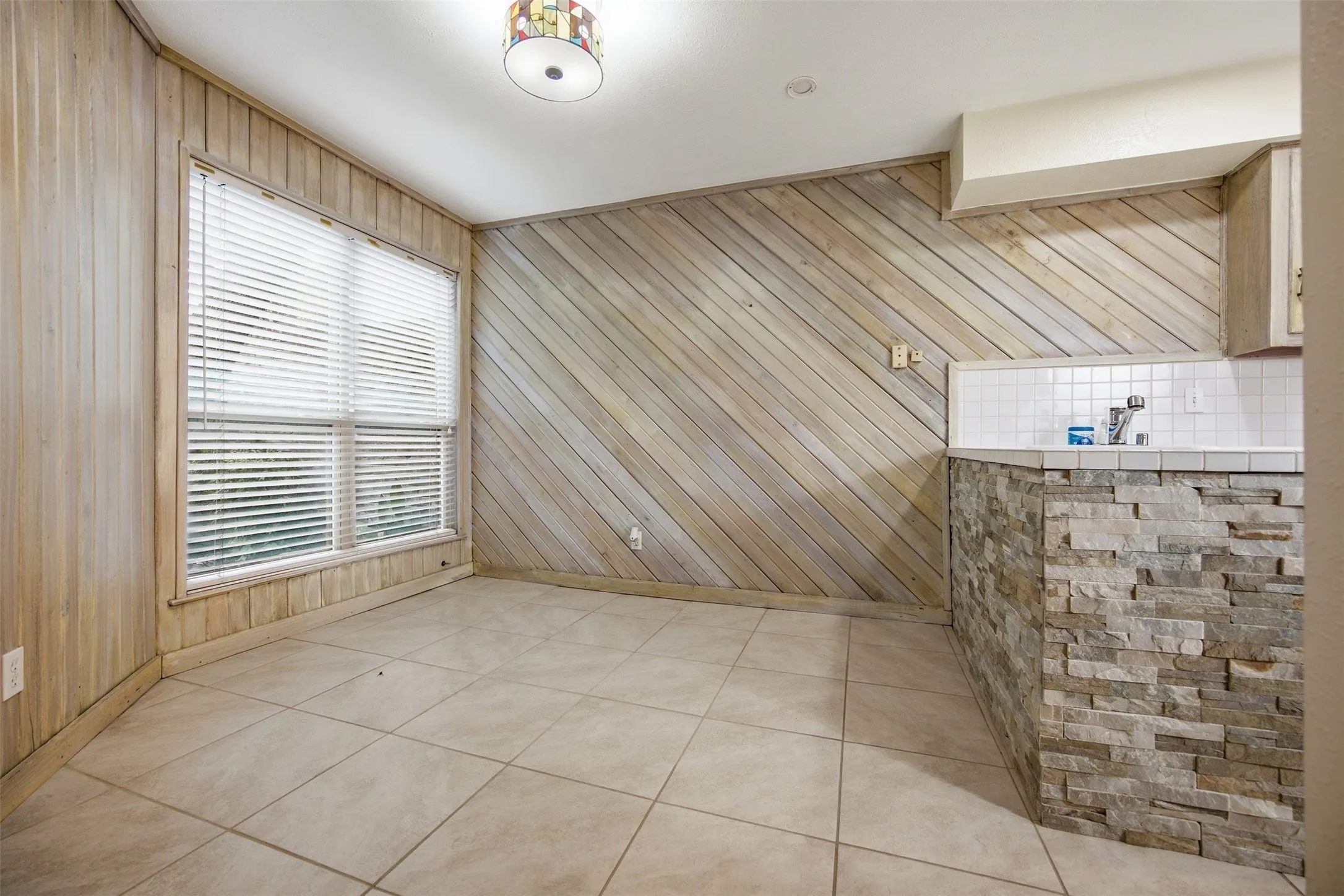 Tile flooring, paneled walls, large window, stone-clad counter base, and tiled backsplash