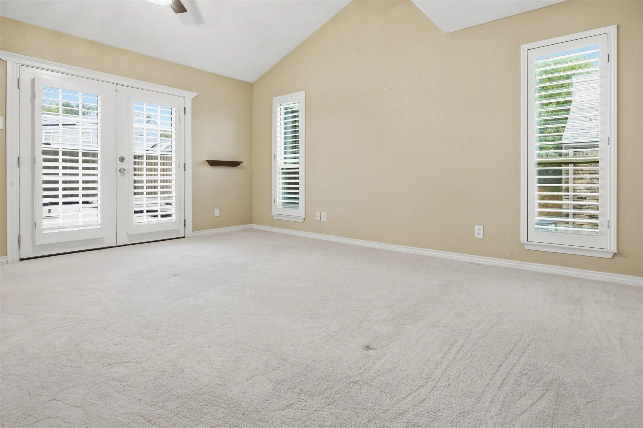 Vaulted ceiling, ceiling fan, carpet flooring, plantation shutters, French doors