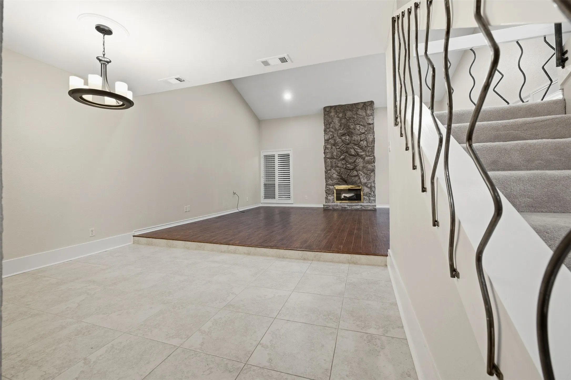Two-story interior with varied flooring, a vaulted ceiling, and a stone fireplace