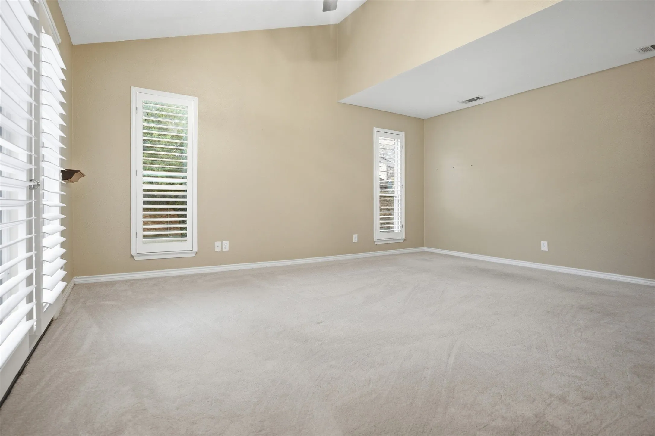Vaulted ceiling, neutral tone walls, white baseboards, white window frames, and plantation shutters