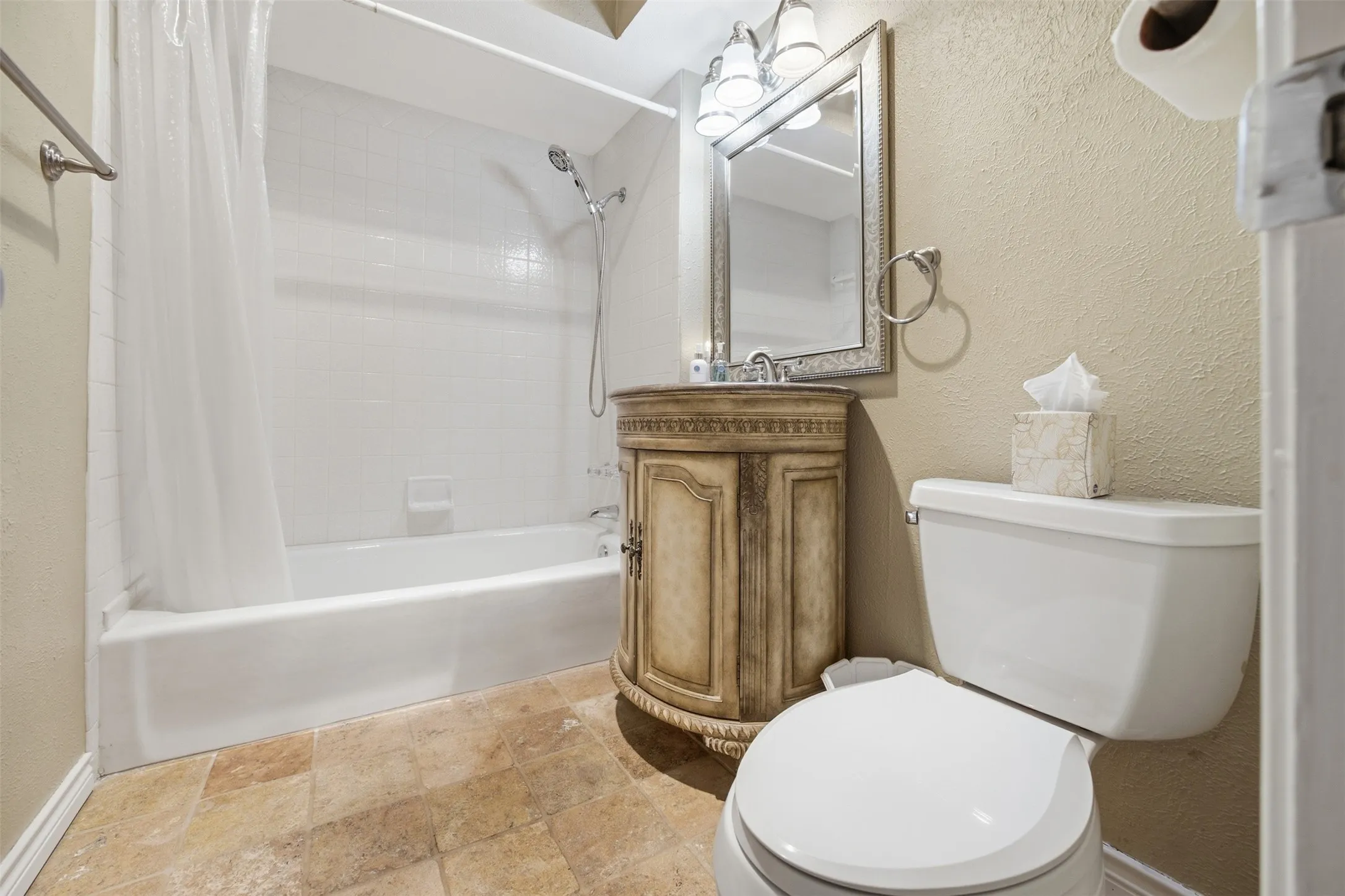 Neutral-toned tile flooring, bathtub with white subway tile surround, vanity with decorative wood-finish cabinetry, framed mirror, and chrome vanity lighting