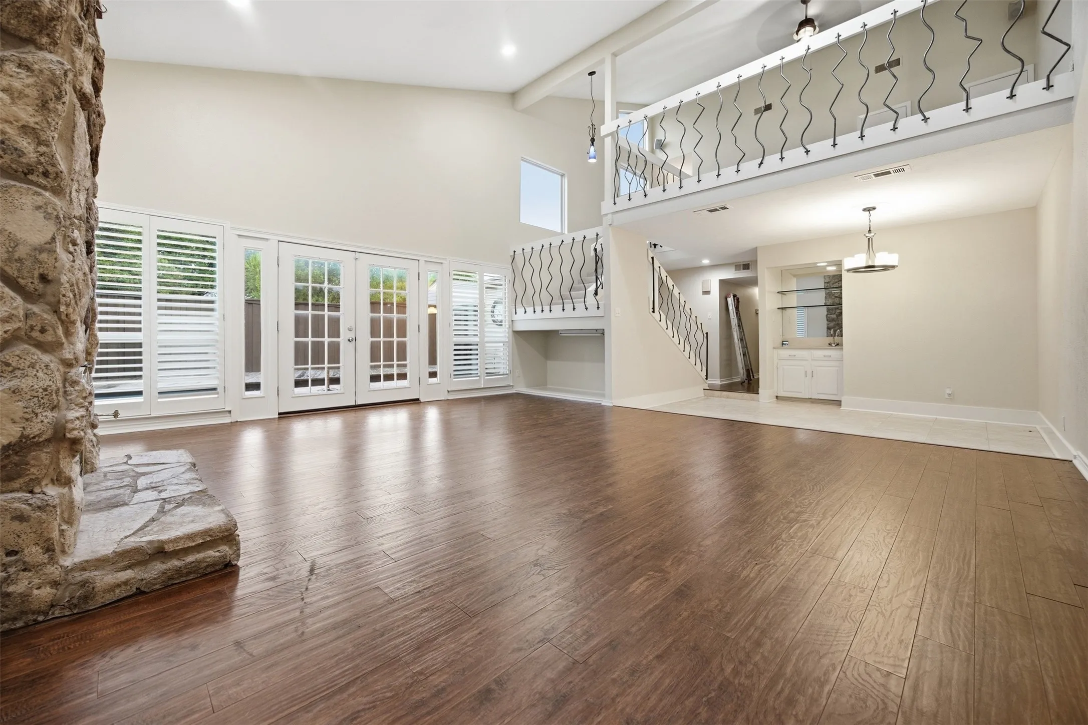 Spacious living area featuring wood-finish flooring, a stone-clad fireplace, and multiple French doors with plantation shutters