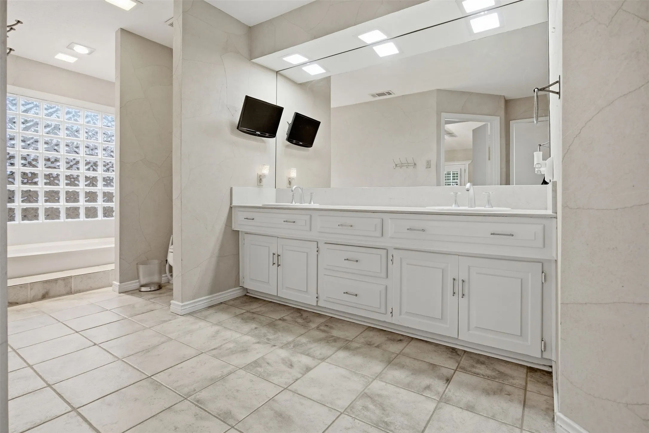 Dual vanity with white cabinetry, integrated sinks, an expansive mirror, and tile flooring