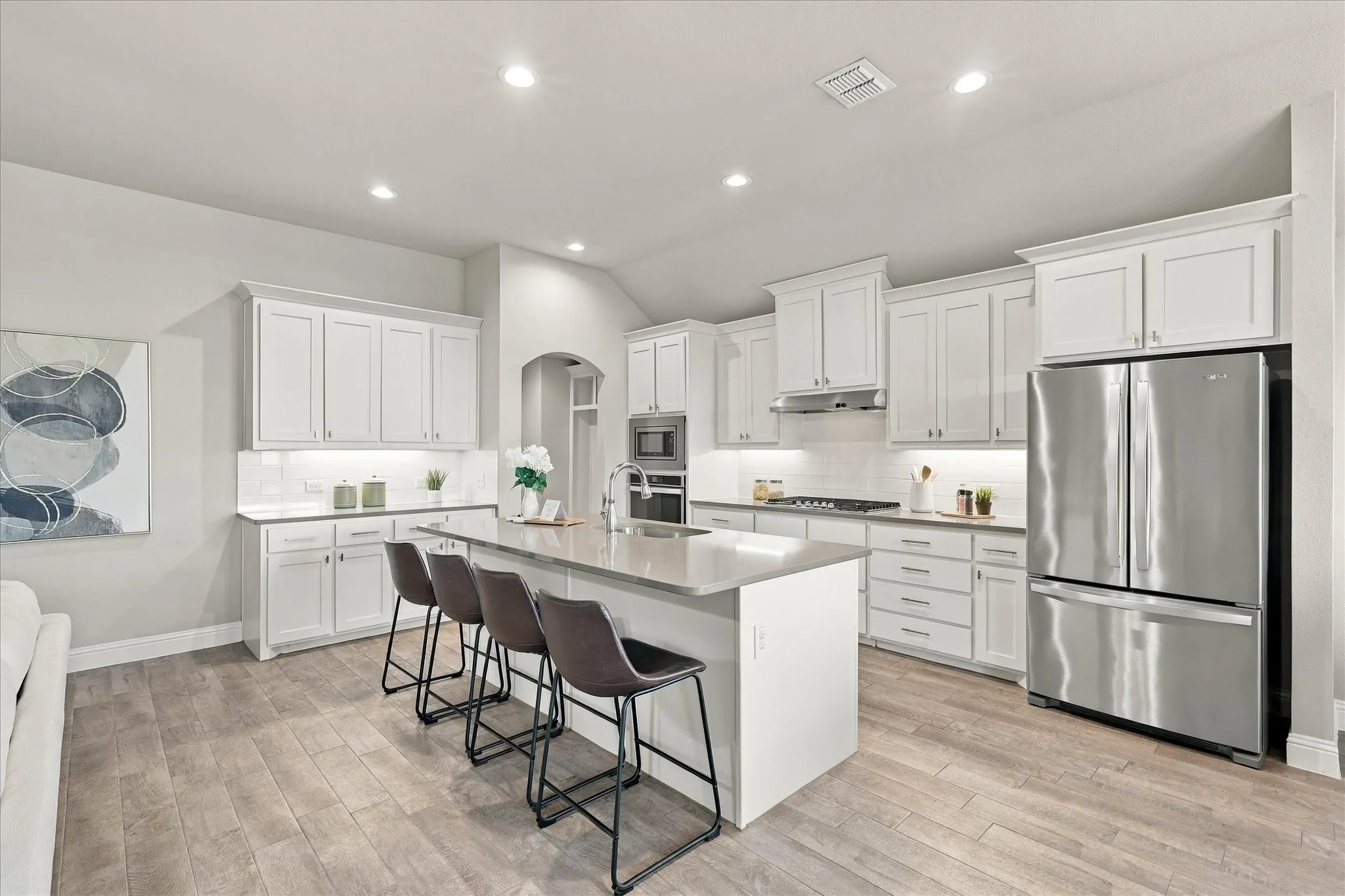 Spacious kitchen with a central island, white cabinetry, integrated stainless-steel appliances, recessed lighting, and wood-finish flooring