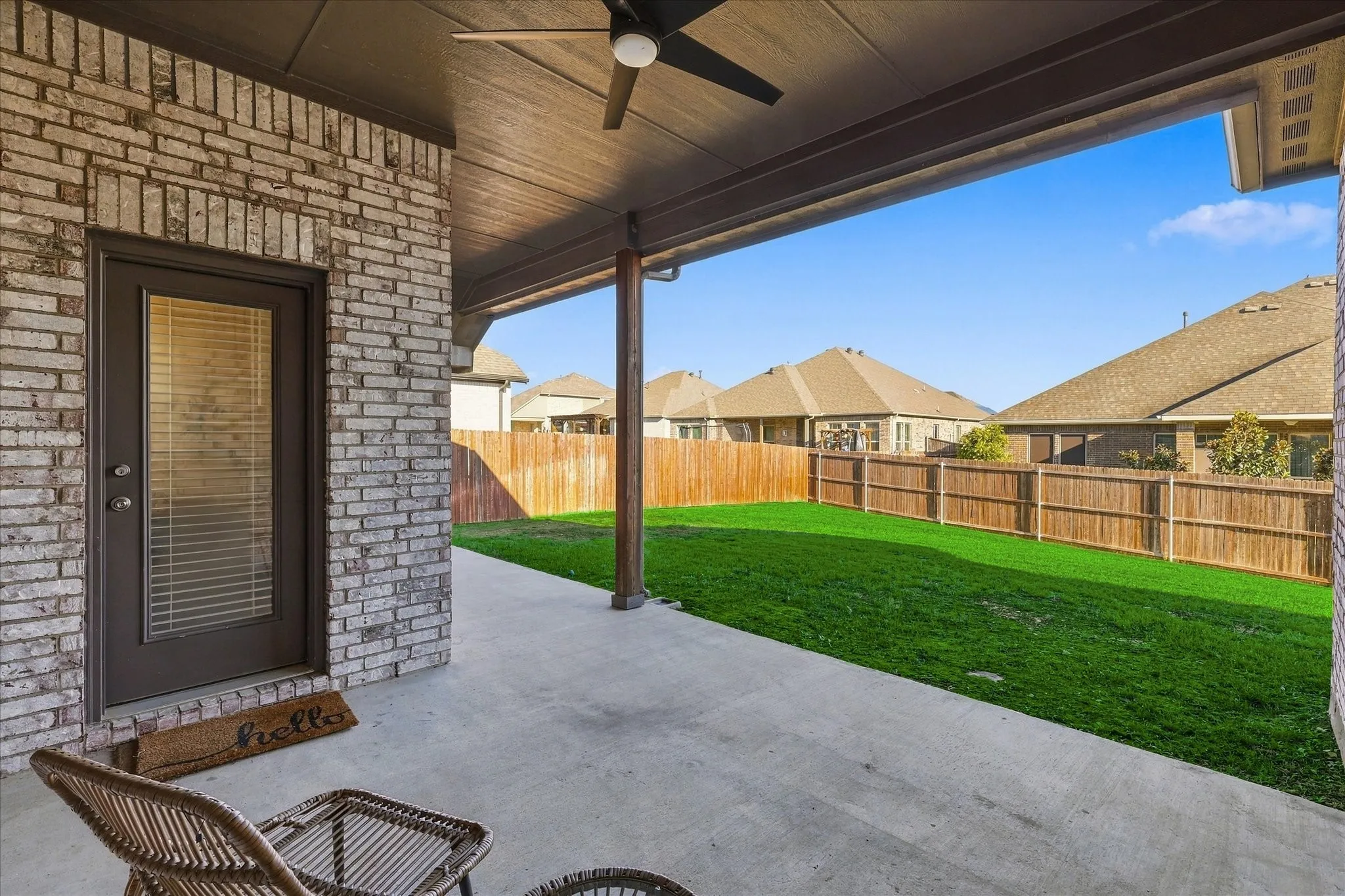 Covered patio with a ceiling fan, concrete flooring, brick exterior, and a wood privacy fence enclosing a grass lawn