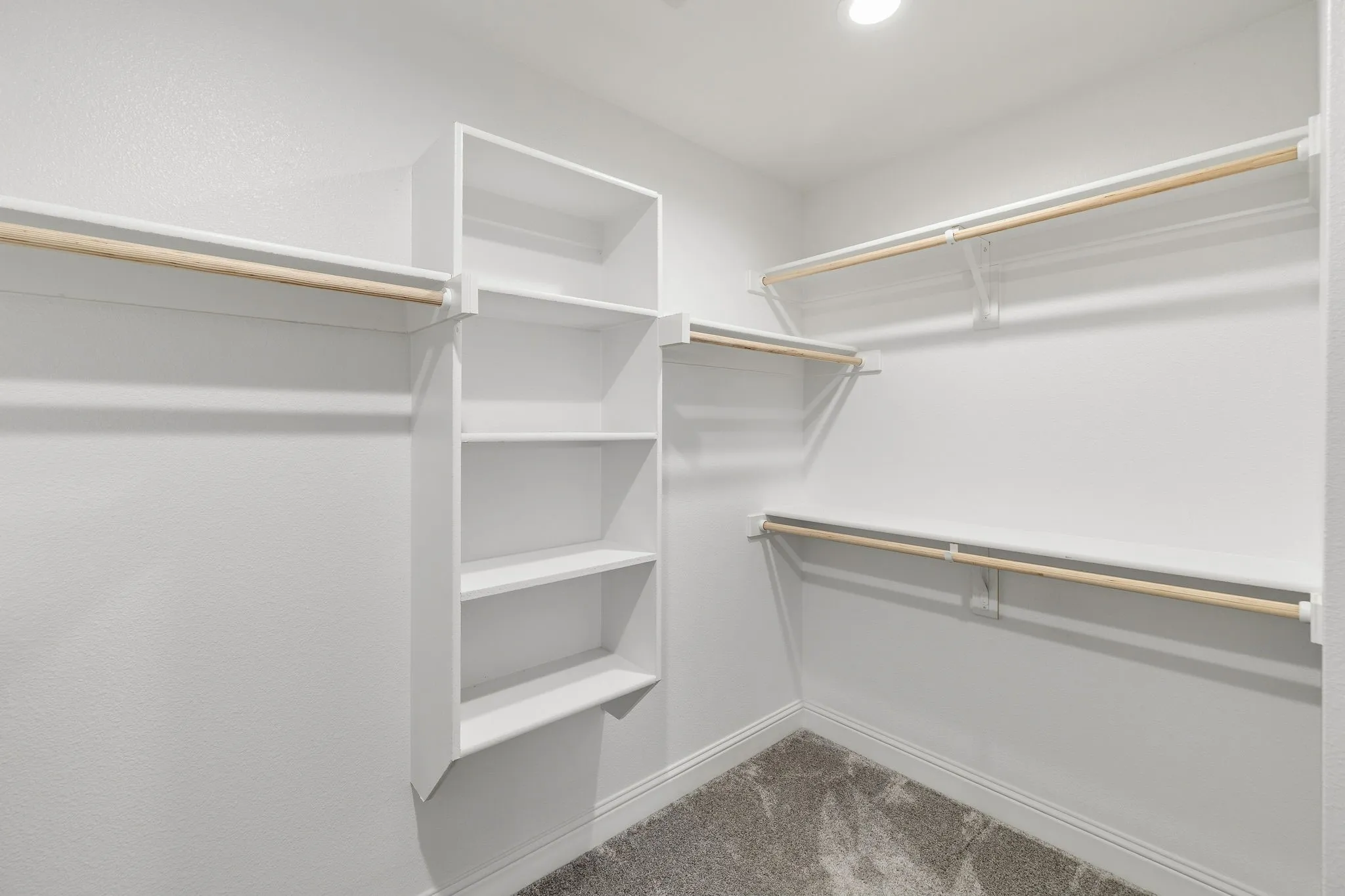 Built-in shelving unit, multiple clothing rods, recessed lighting, and carpet flooring