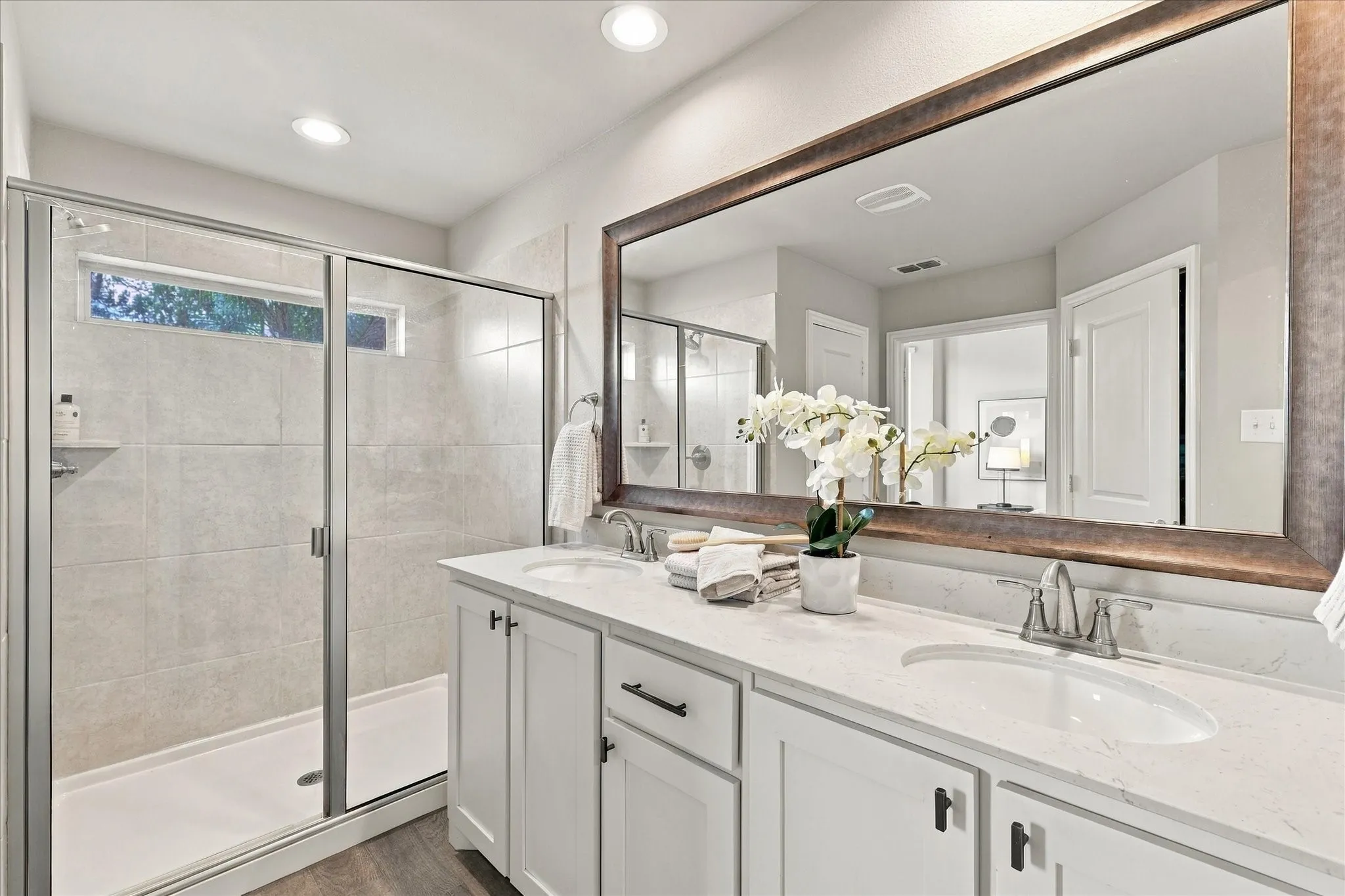 Dual vanity with white cabinetry and integrated sinks, a large framed mirror, and a glass-enclosed shower with tiled walls