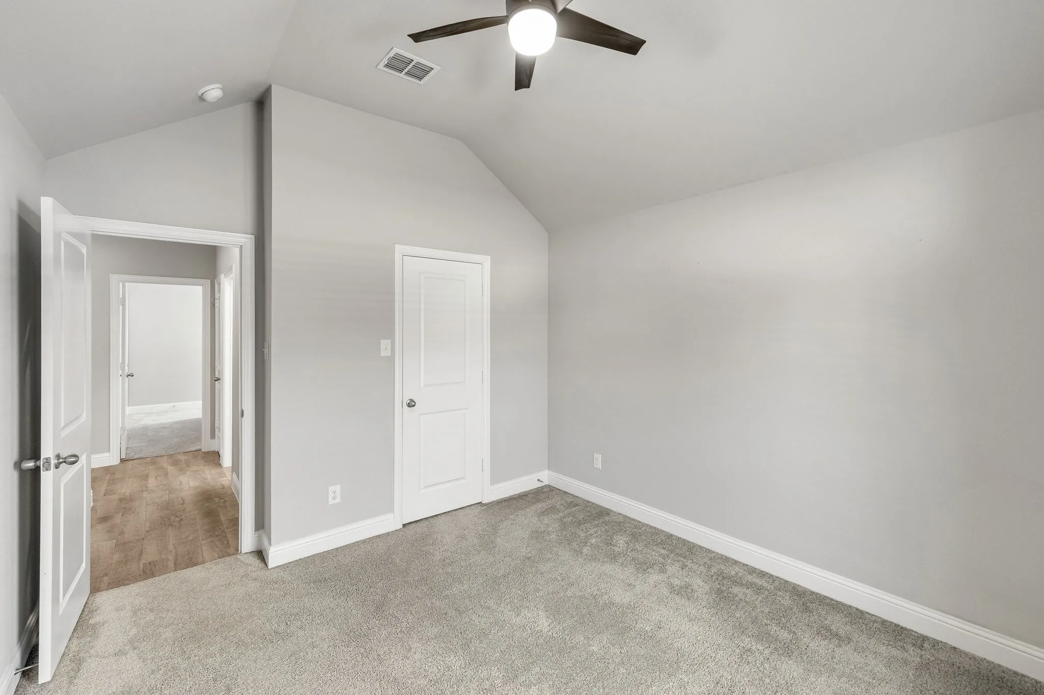 Vaulted ceiling with an attached ceiling fan, light gray wall paint, and gray carpet flooring