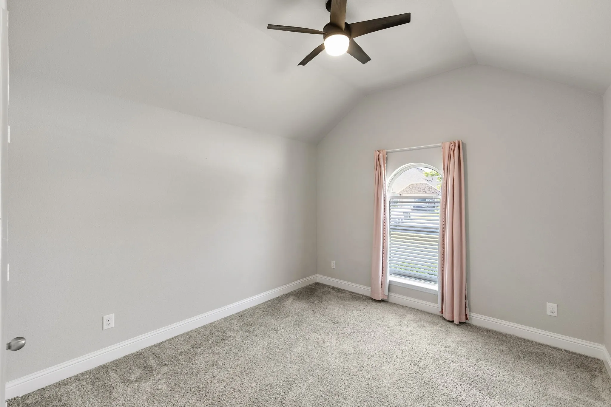Vaulted ceiling with an attached ceiling fan, arched window with horizontal blinds, and gray carpeting