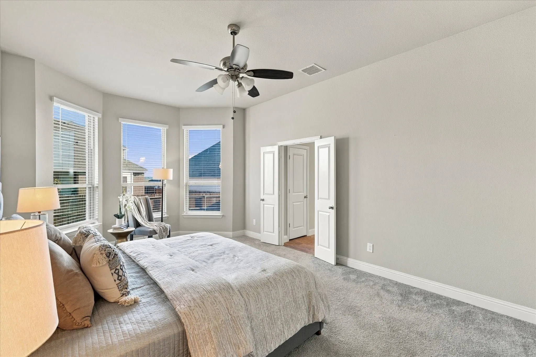 Bay window with three windows, gray carpet flooring, ceiling fan with light fixture, and white bi-fold doors