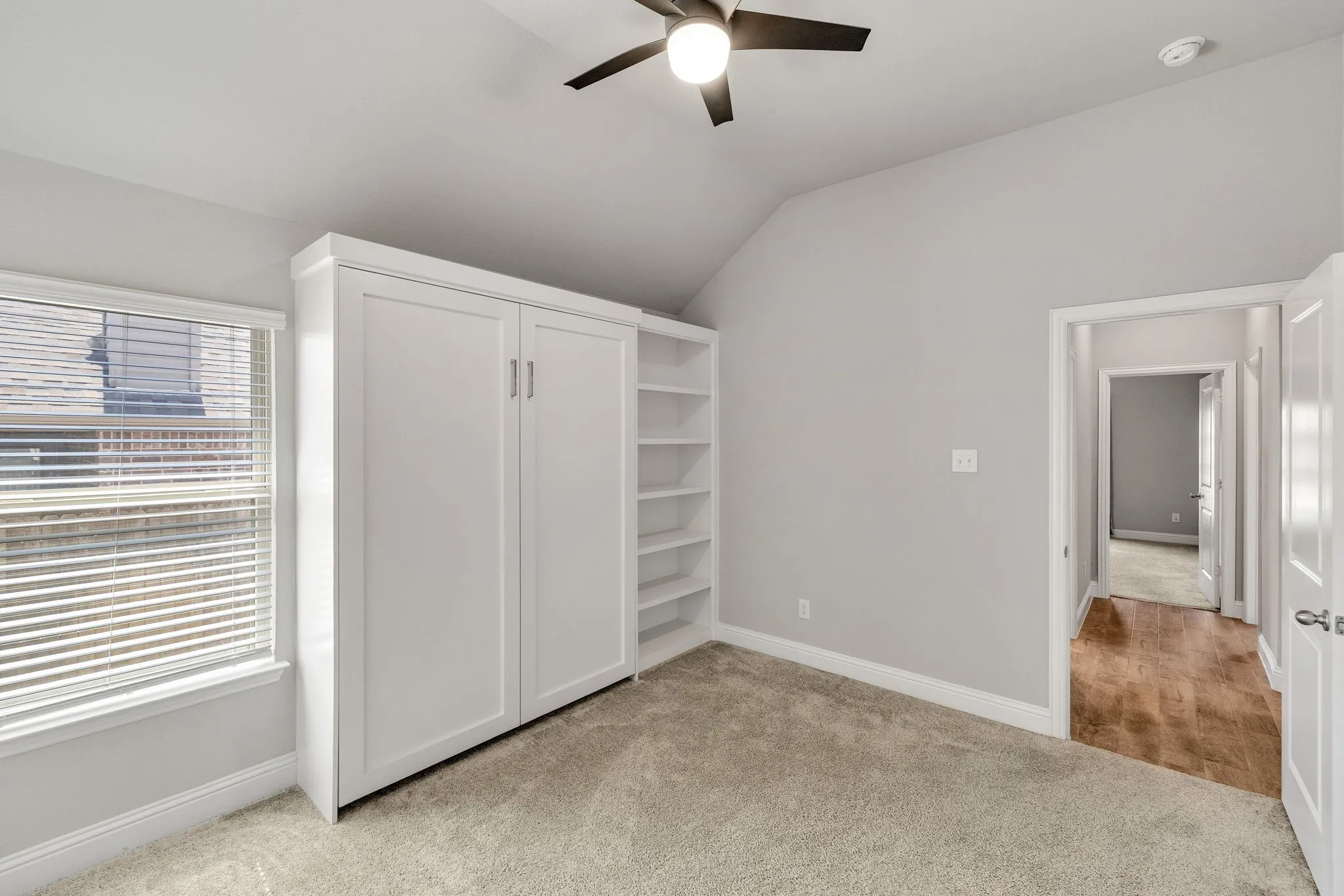 Built-in cabinetry with integrated shelving, vaulted ceiling, ceiling fan, and window with blinds