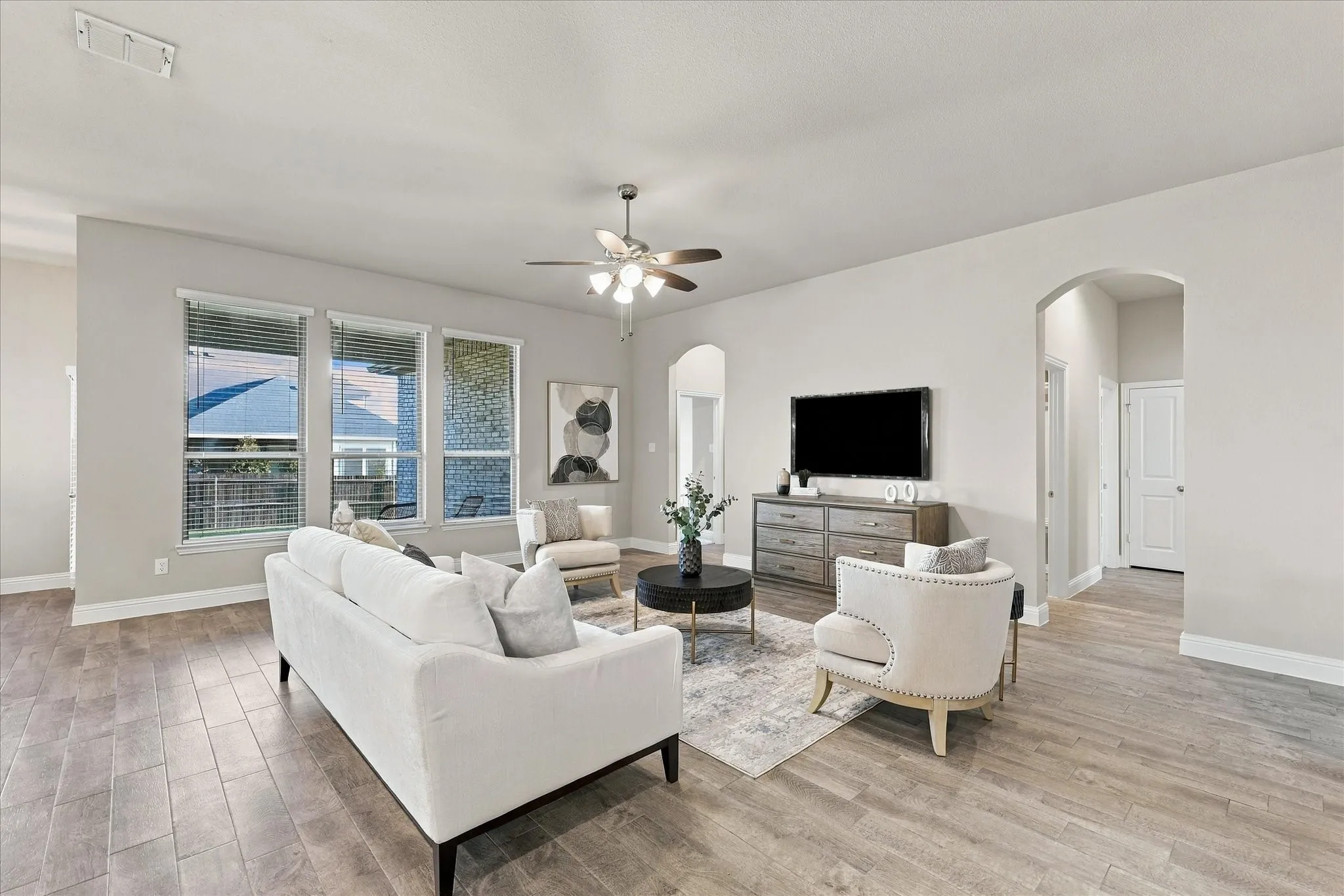 Spacious living area featuring wood-finish flooring, a ceiling fan, and multiple windows with blinds