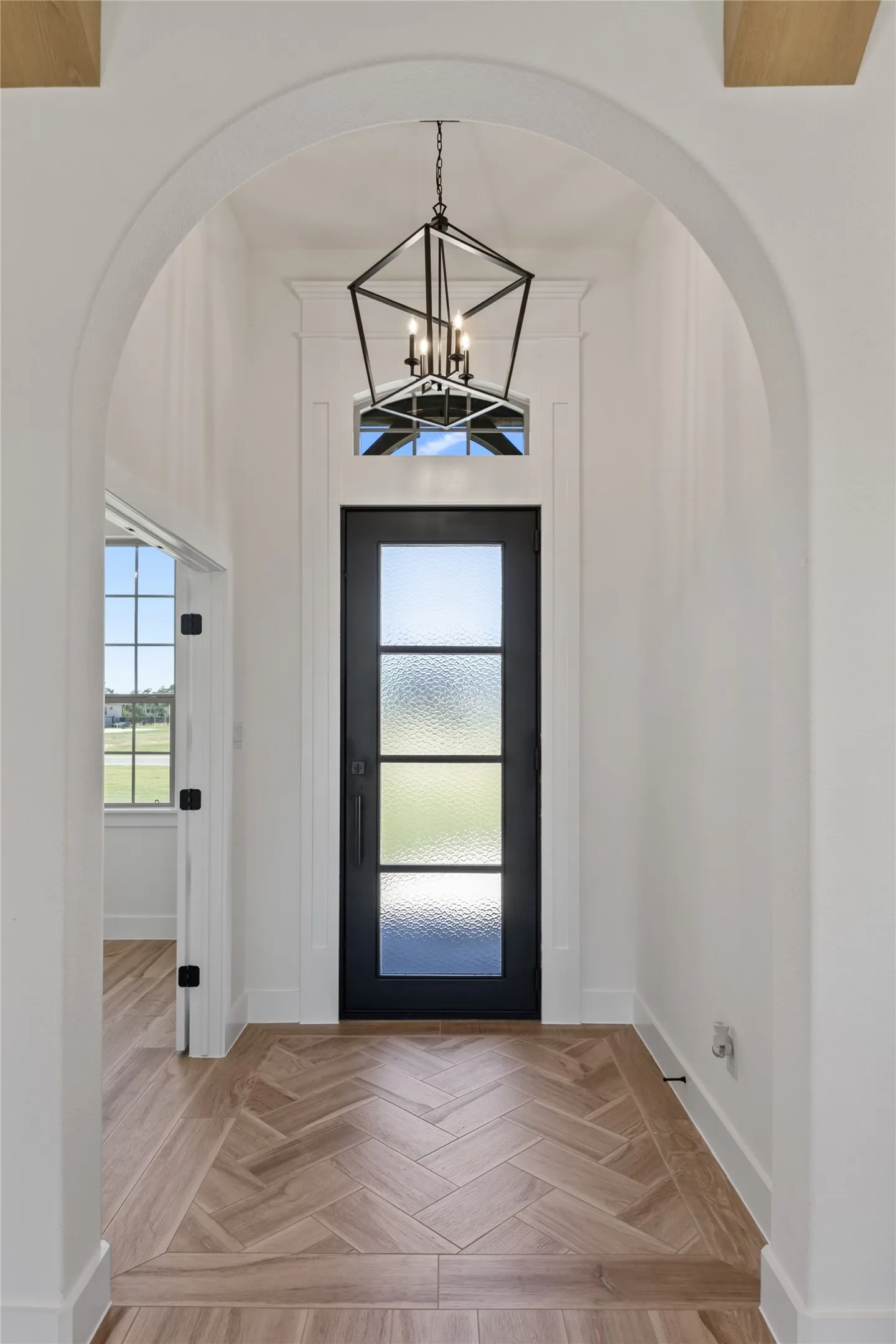 Arched entryway with a black multi-paneled door, transom window, and an overhead geometric chandelier