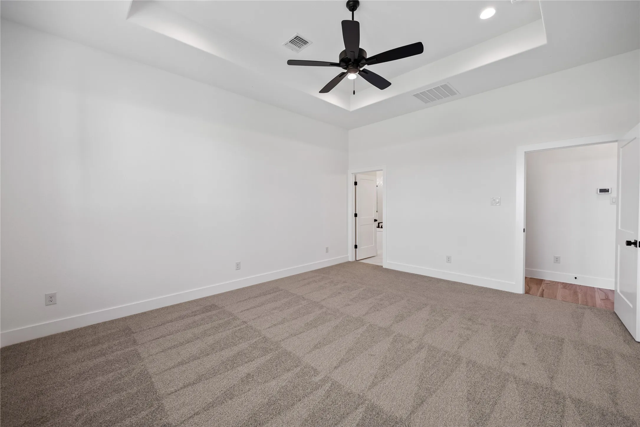 Spacious room featuring tray ceiling with recessed lighting, ceiling fan, neutral carpeting, and white walls