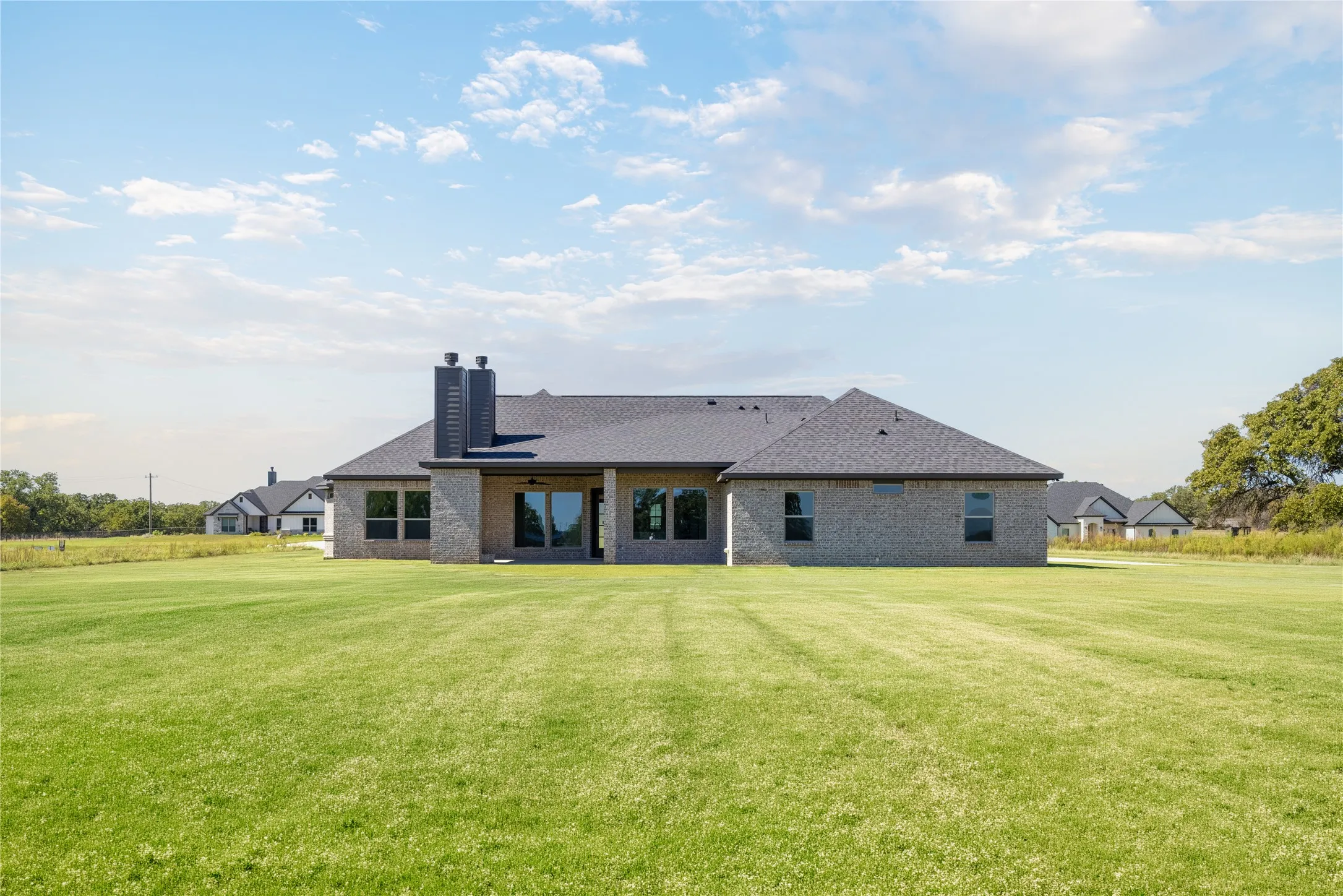 Expansive green lawn with a newly constructed brick exterior, dark shingle roof, and multiple large windows