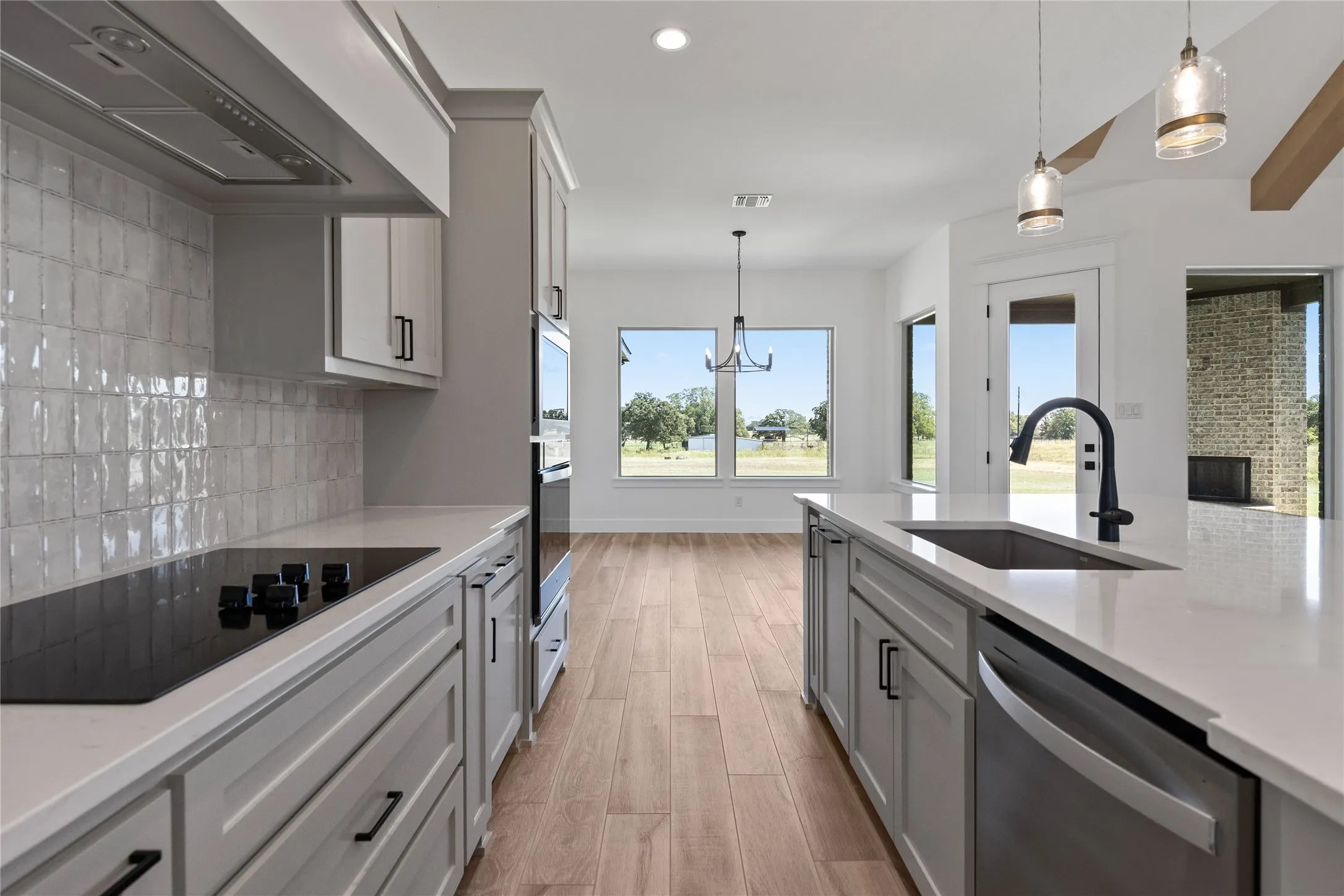 Modern kitchen featuring an integrated electric cooktop, light-toned cabinetry, and a central island with an undermount sink