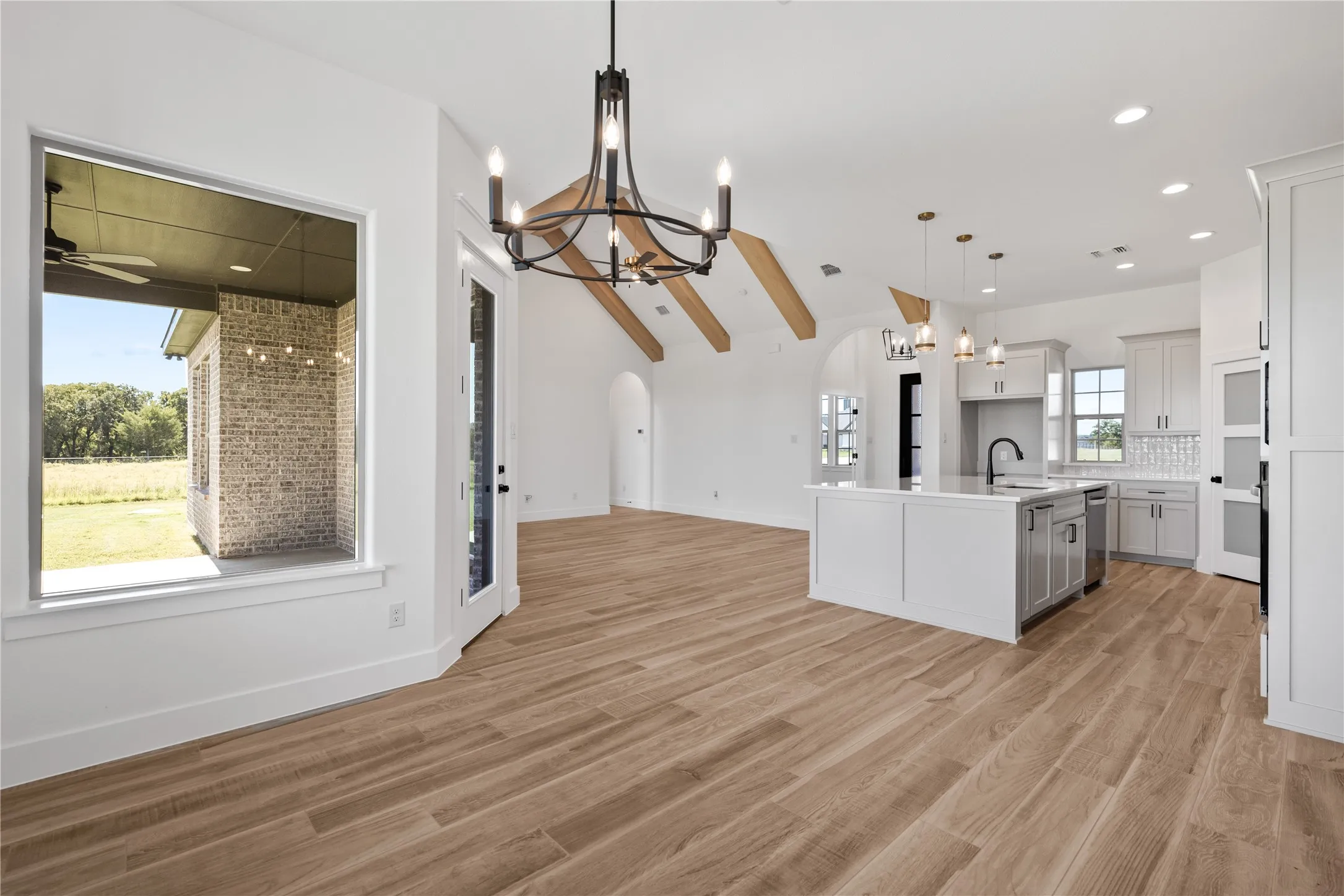 Open concept living space featuring wood-finish flooring, vaulted ceilings with exposed beams, and a kitchen island with a built-in sink