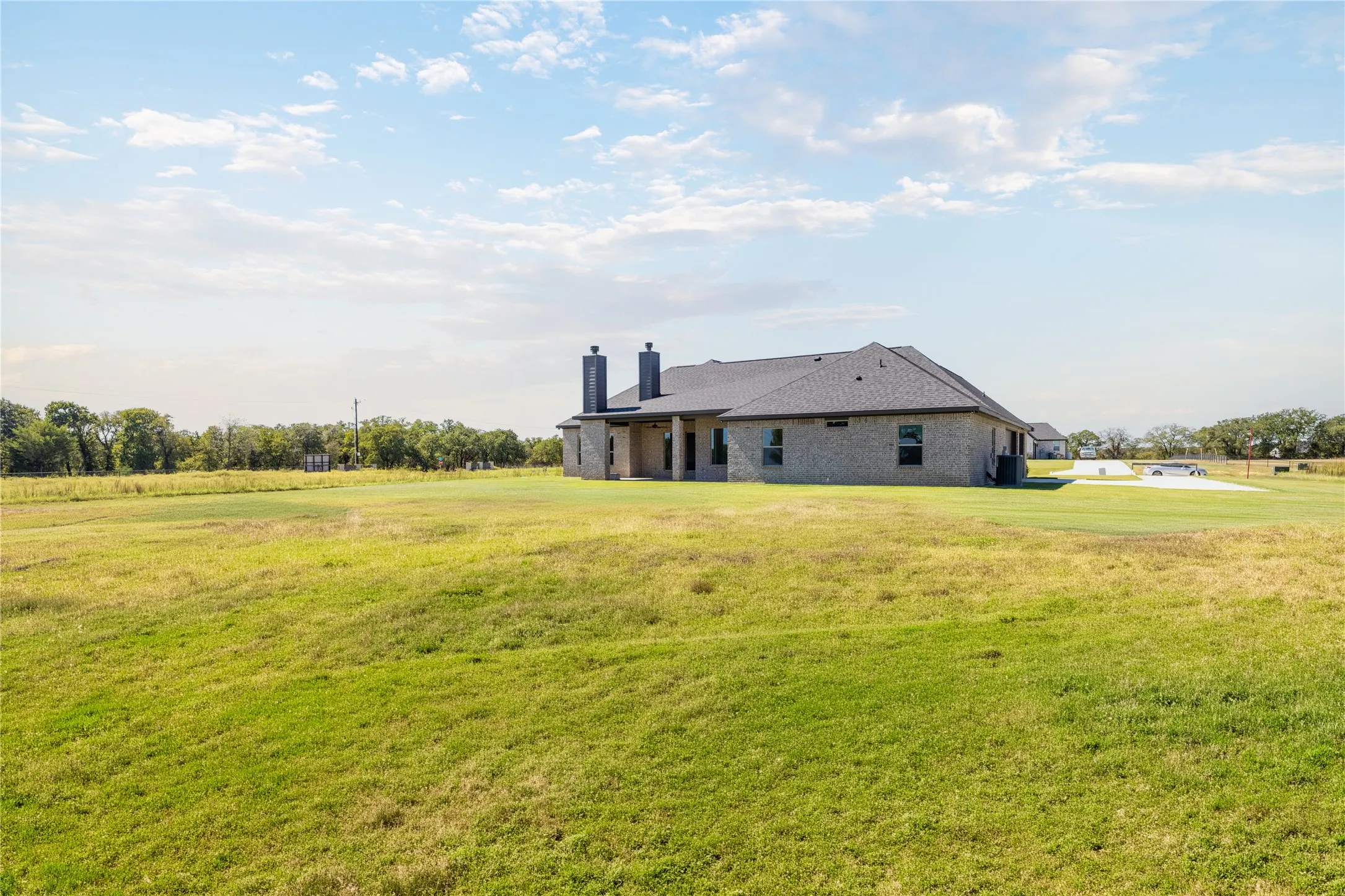 Expansive property featuring a brick exterior, dark-toned roof, multiple chimneys, and a large grassy area