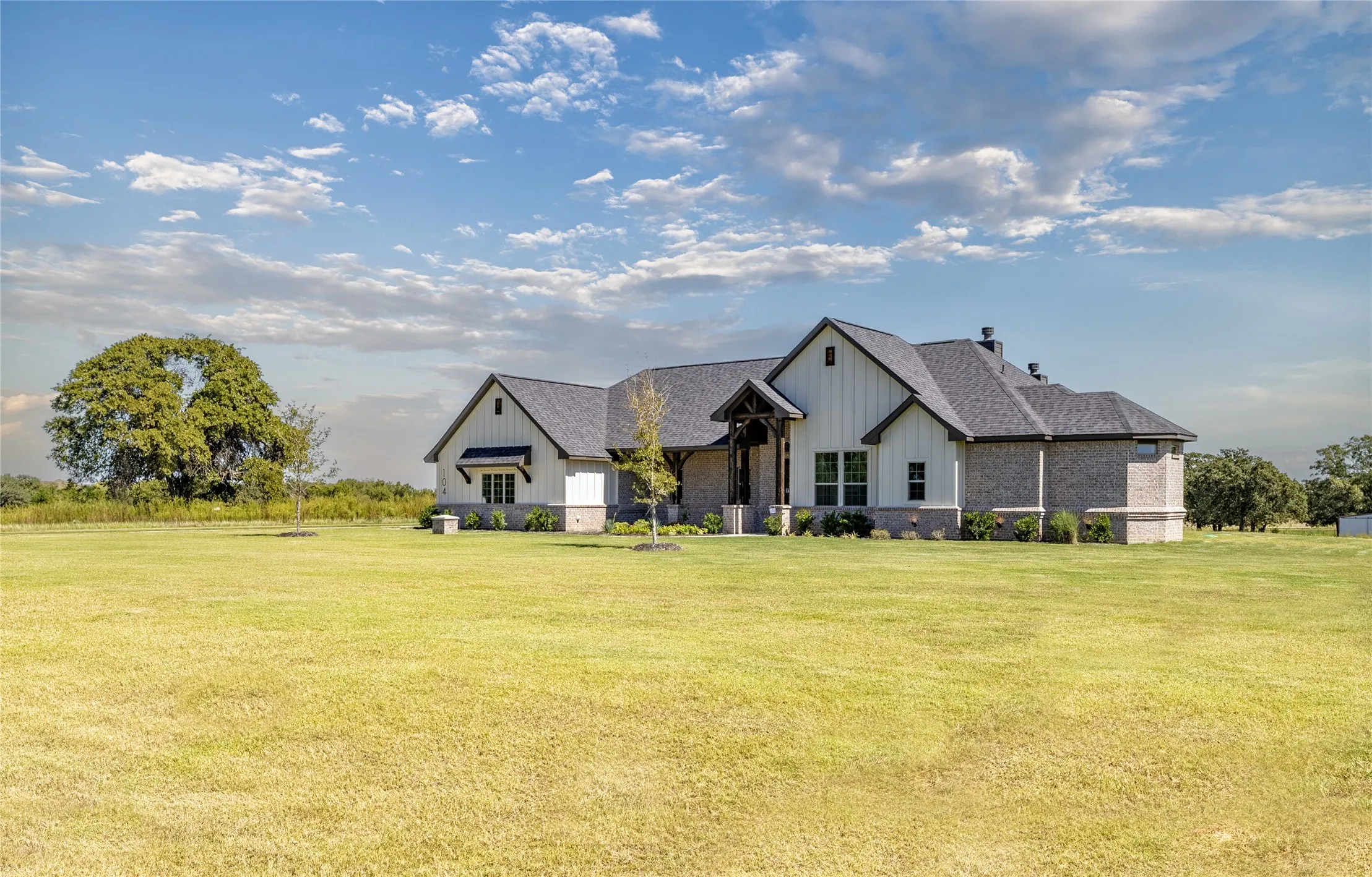 Ranch-style residence featuring a combination of brick and vertical siding, a dark shingled roof, a covered entryway with exposed wood beams, and a landscaped foundation