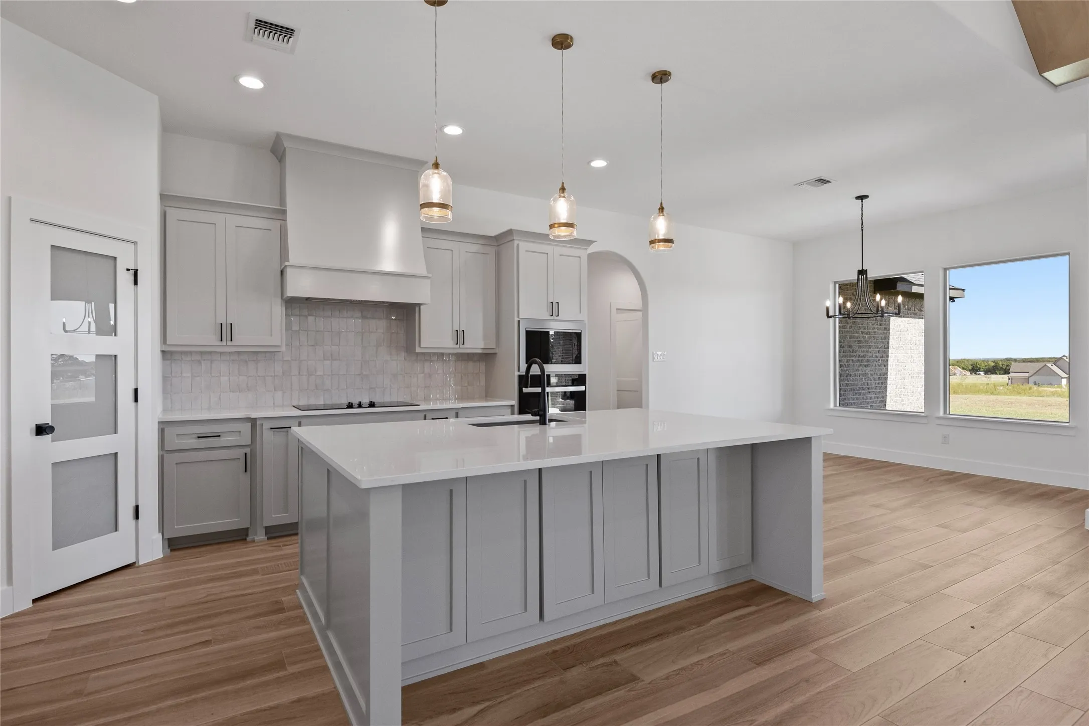 Kitchen featuring a large island with white countertop, light gray cabinetry, built-in appliances, and wood-finish flooring