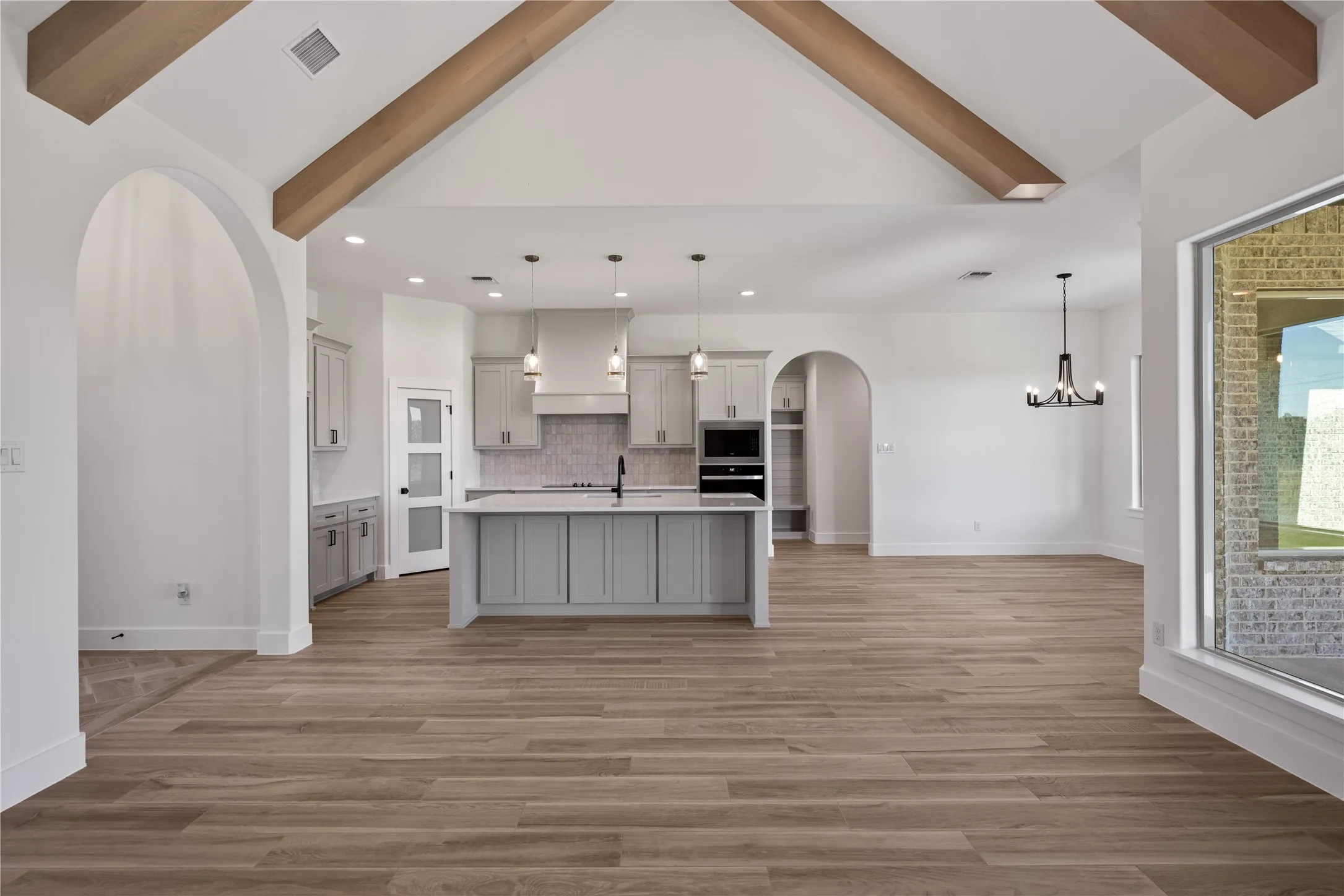 Vaulted ceiling with exposed wood beams, wood-finish flooring, recessed lighting, arched doorways, and a large window