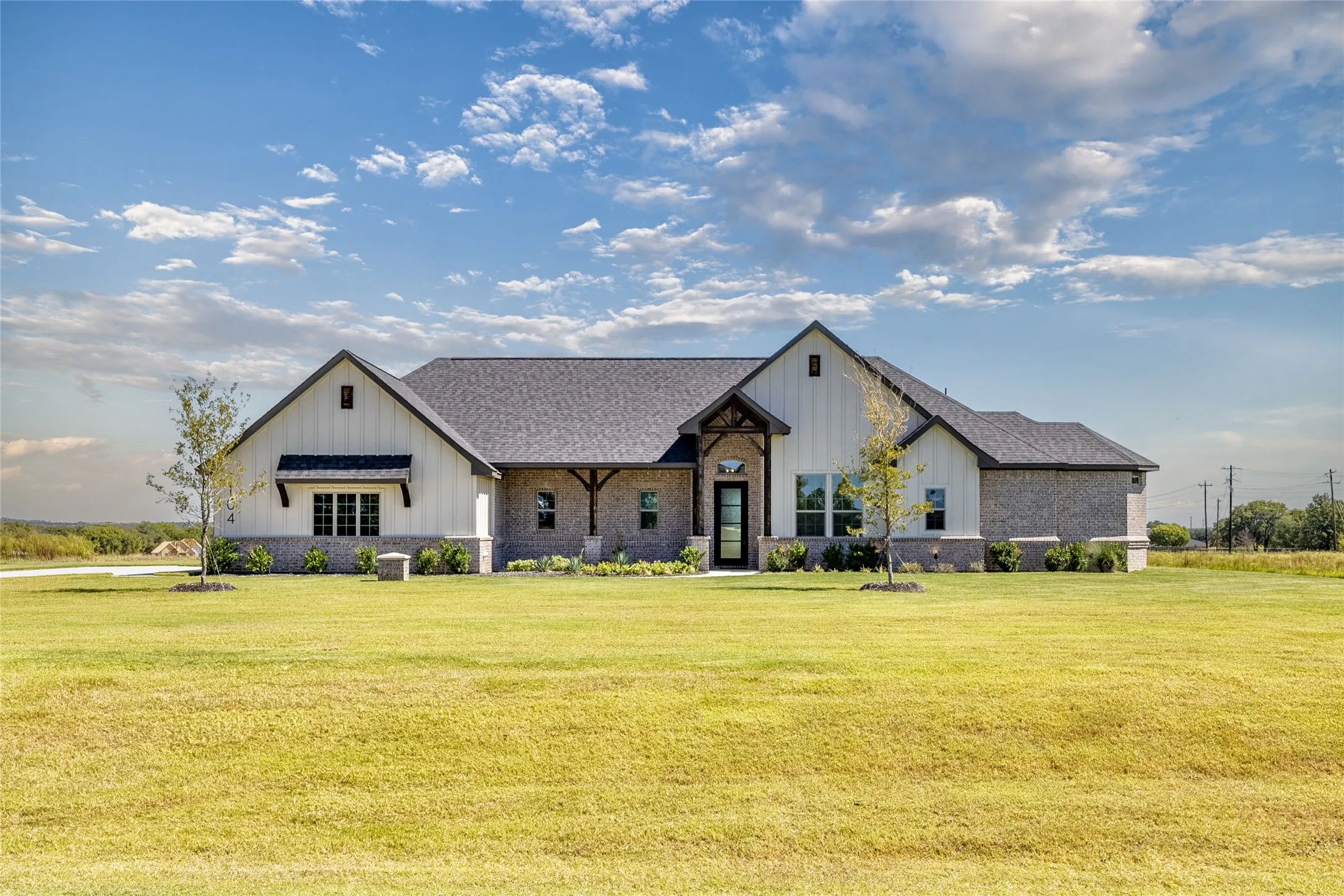 Modern farmhouse exterior with board and batten siding, brick accents, dark-framed windows, a covered front entry, and a dark shingle roof