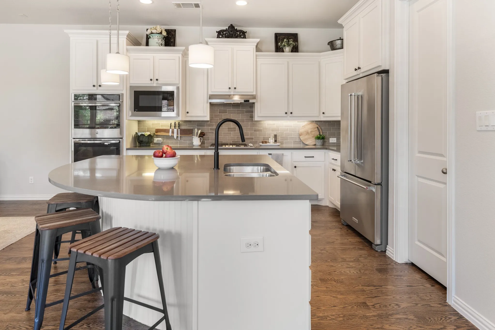 Kitchen featuring white cabinetry, stainless steel appliances, a center island with a sink, pendant lighting, and wood-finish flooring