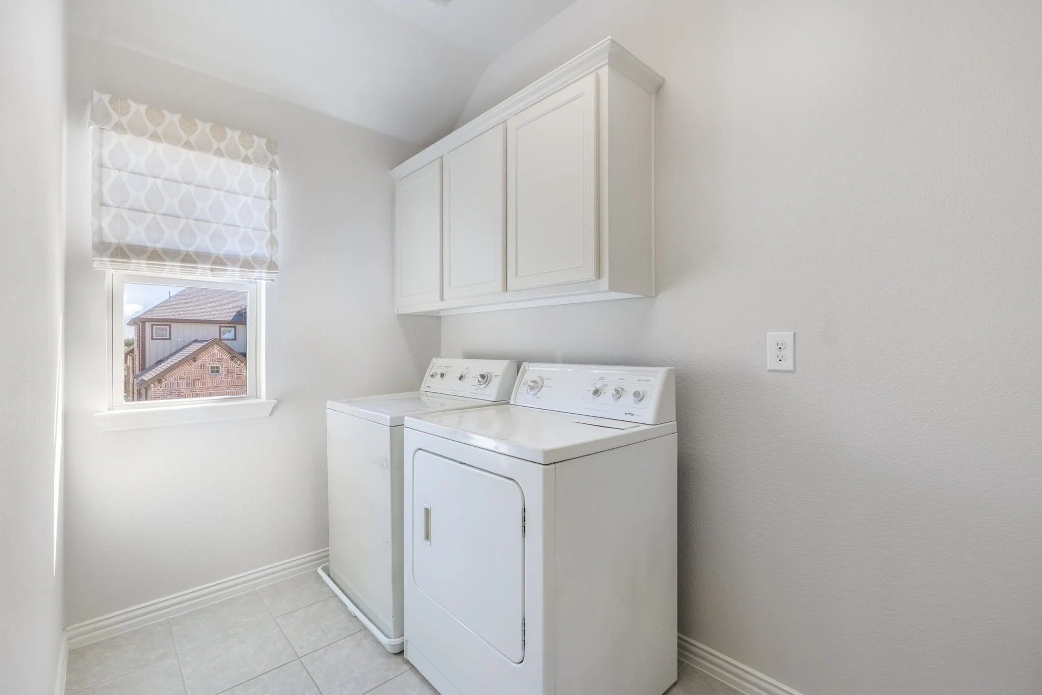 White shaker-style cabinetry with crown molding, a window with a patterned Roman shade, and tiled flooring