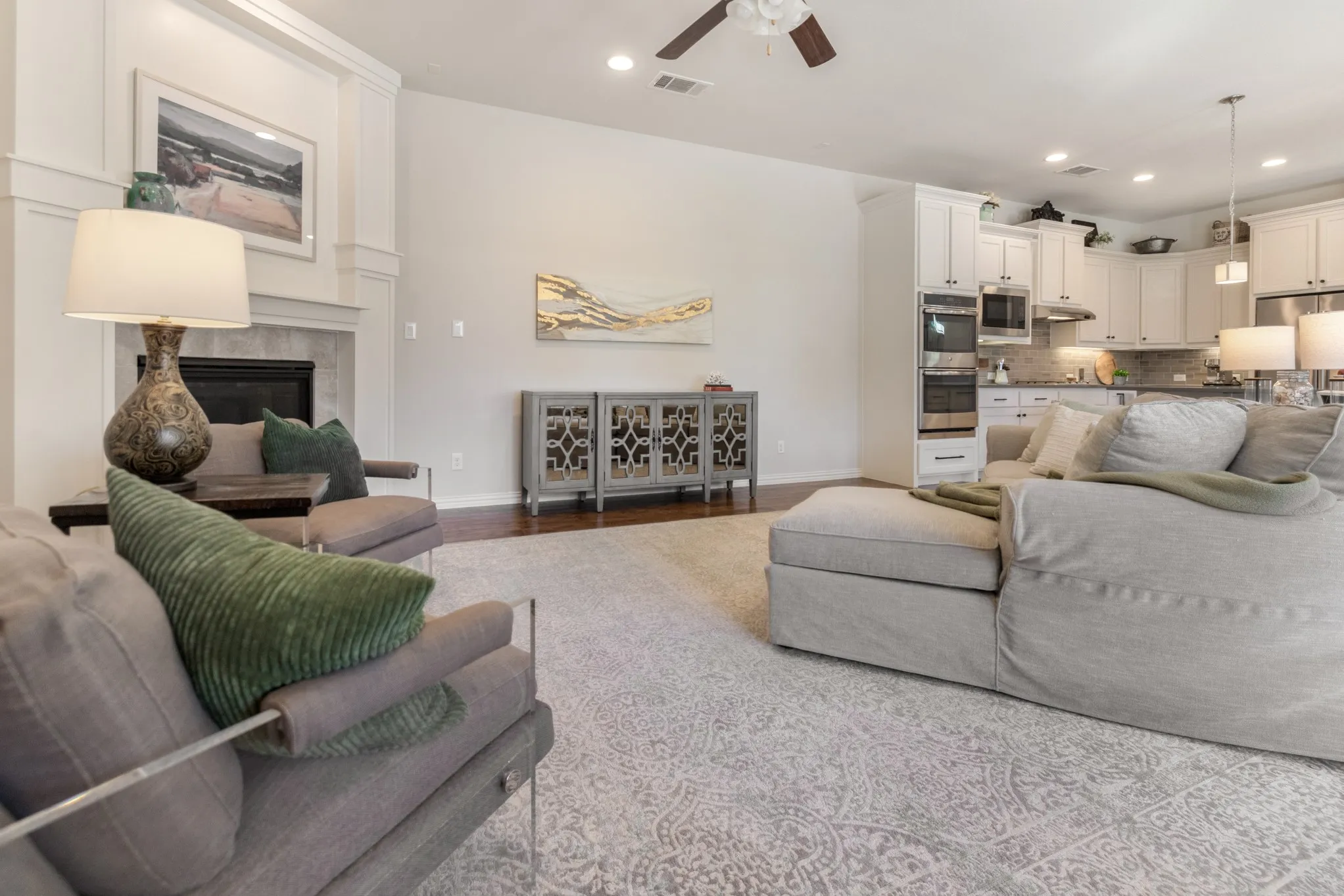 Hardwood-style flooring, white built-in cabinetry, recessed lighting, ceiling fan, and a fireplace with a stone surround