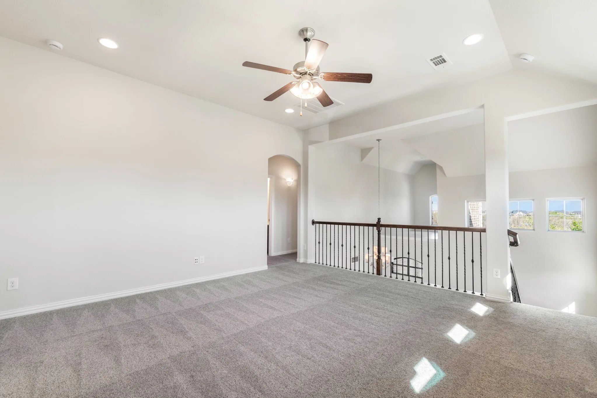 Expansive carpeted loft with recessed lighting, ceiling fan, and wrought iron balustrade